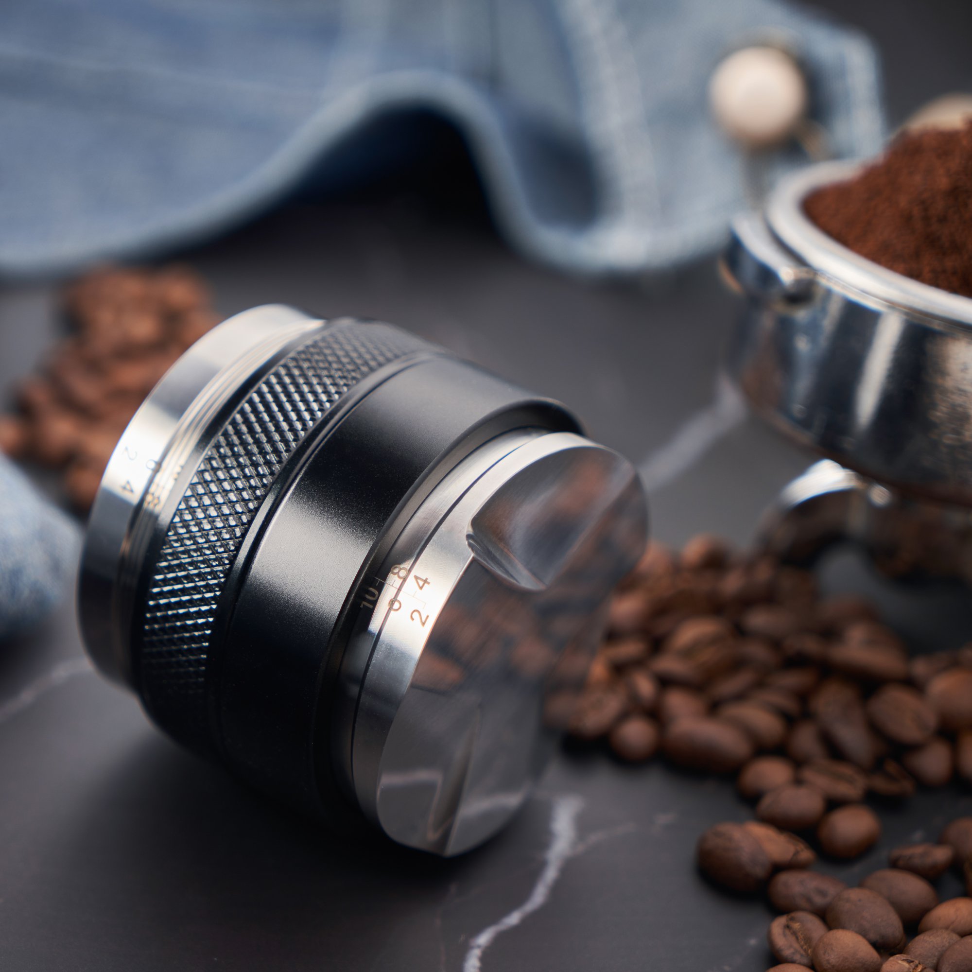 Coffee grinder with coffee beans and ground coffee around it on a dark surface.