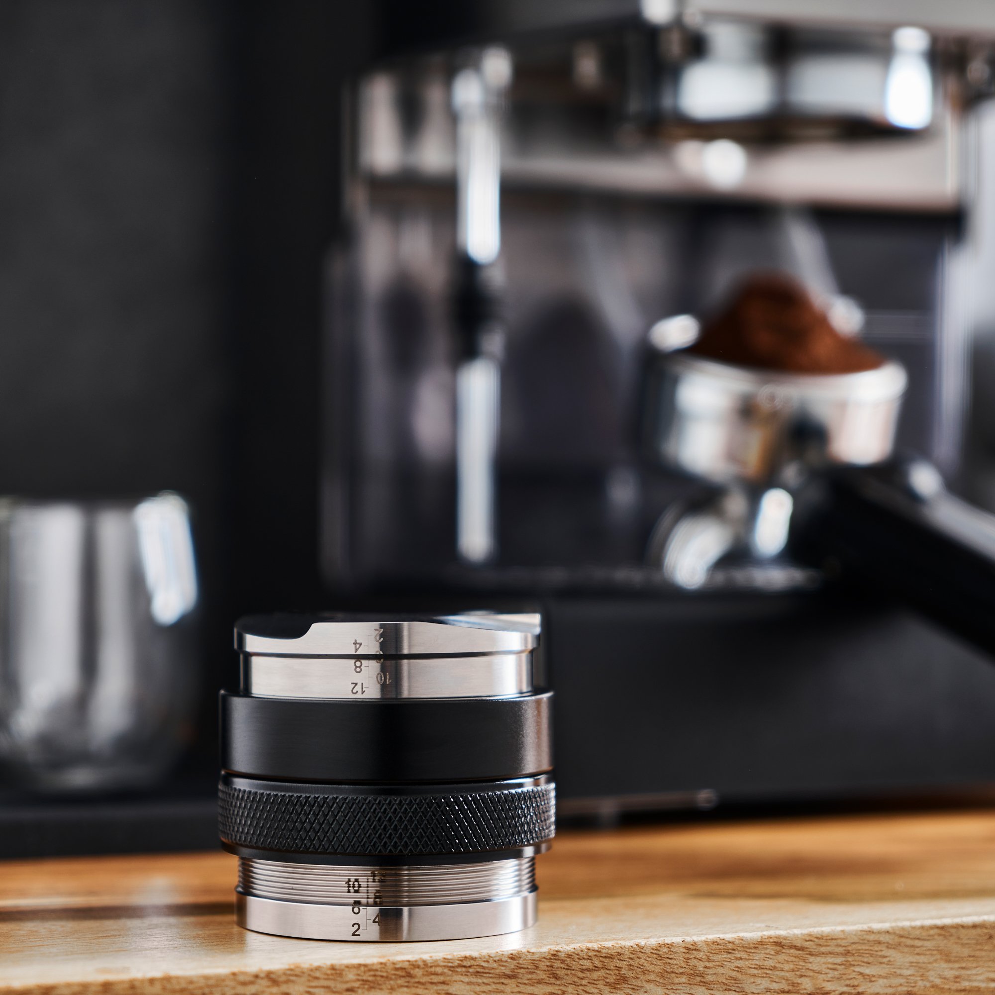 A coffee timer on a wooden surface in front of a shiny espresso machine with a portafilter filled with ground coffee