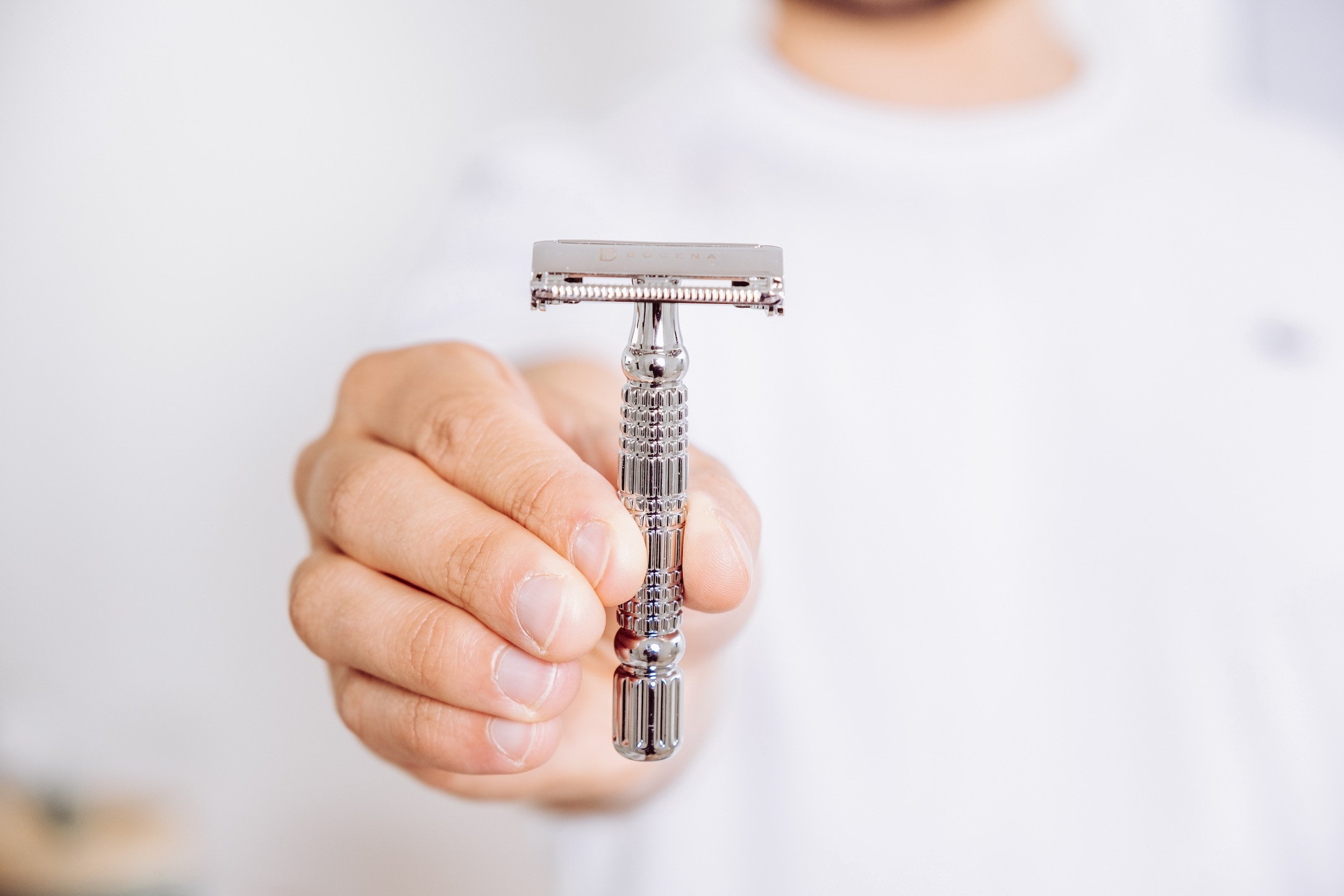 A hand holding a traditional safety razor with a metal handle and a straight razor head.
