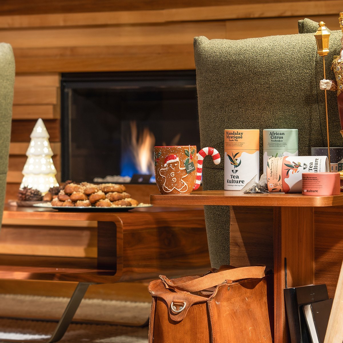 Cozy living room with a fireplace, decorated for Christmas with a gingerbread cookie mug, candies, and tea on a table.