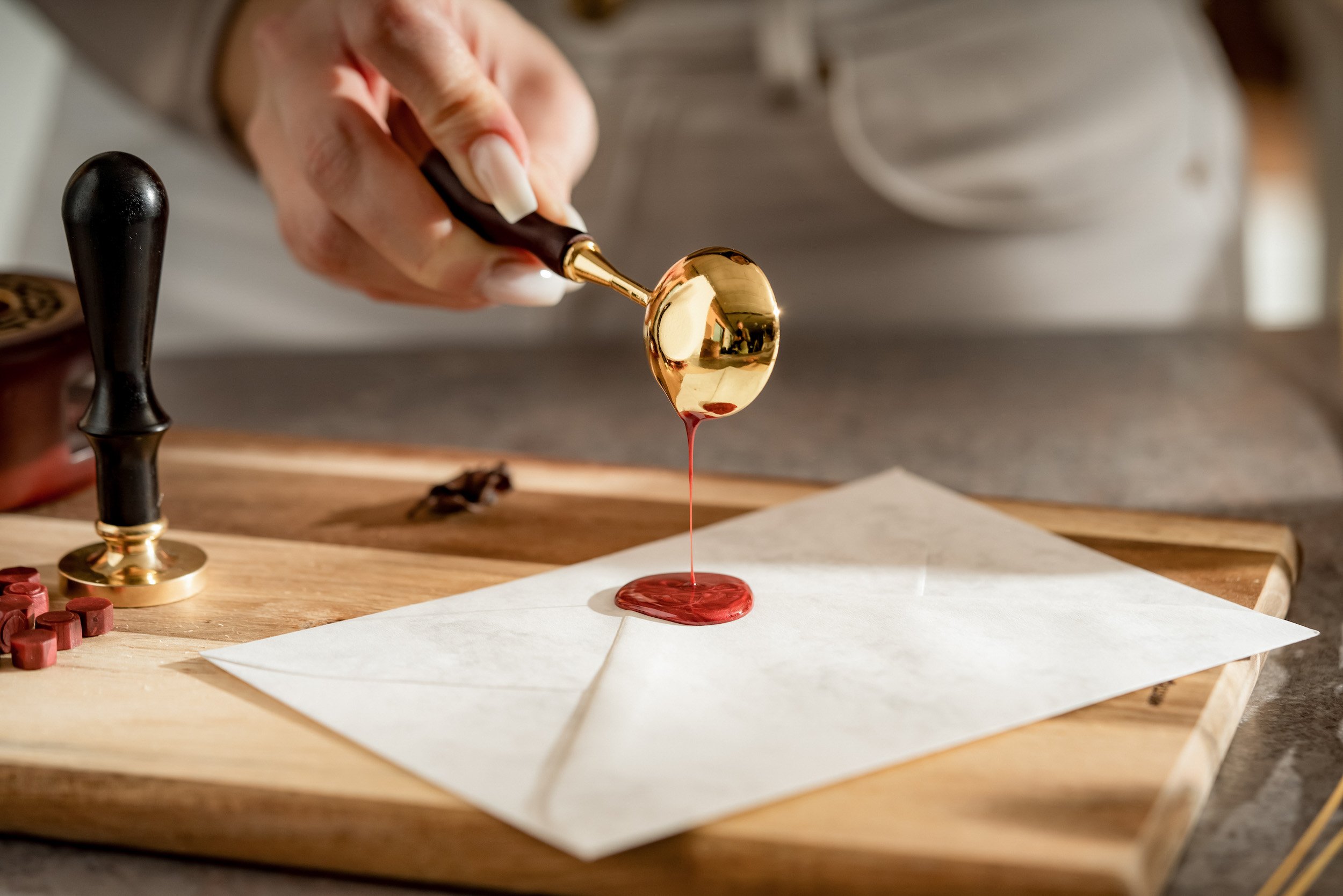 Close-up of a person using a wax seal stamp to seal an envelope with red wax on a wooden table.