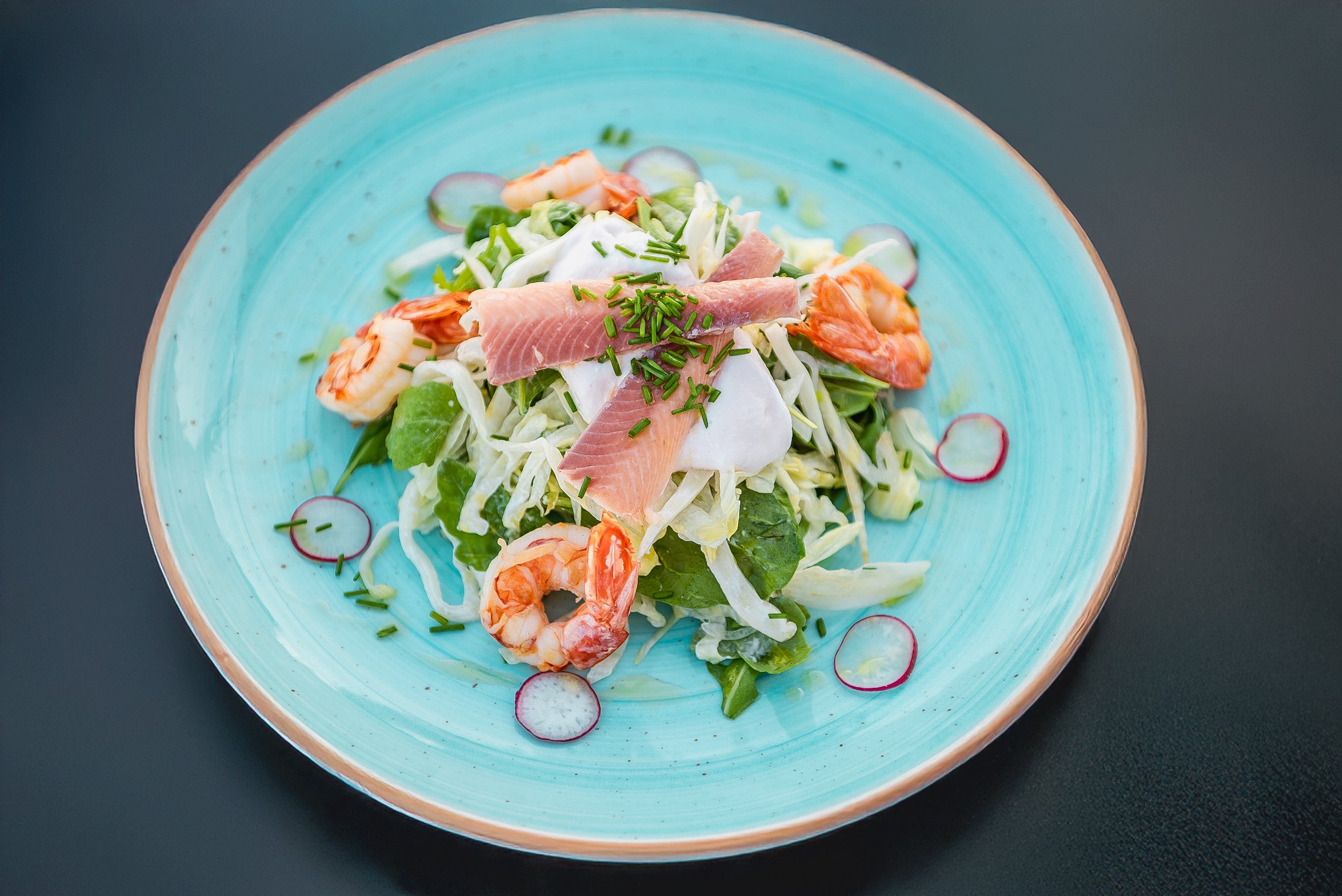 Seafood salad with shrimp, smoked salmon, lettuce, radish slices, and chives on a turquoise plate.