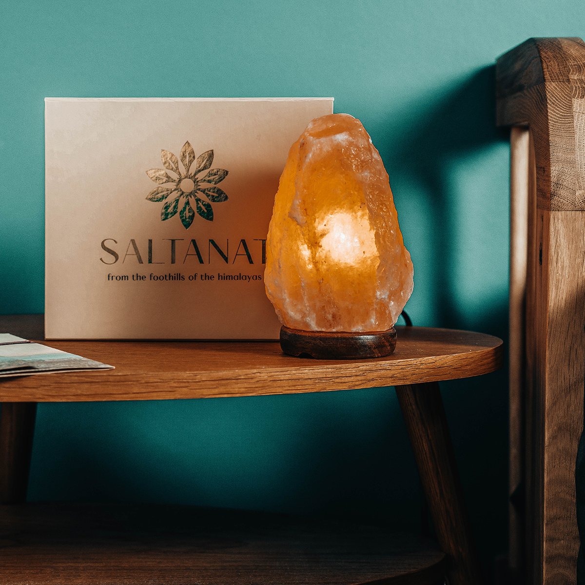 Salt lamp on a wooden table next to a box labeled Saltanat from the foothills of the Himalayas, with a teal wall in the background.