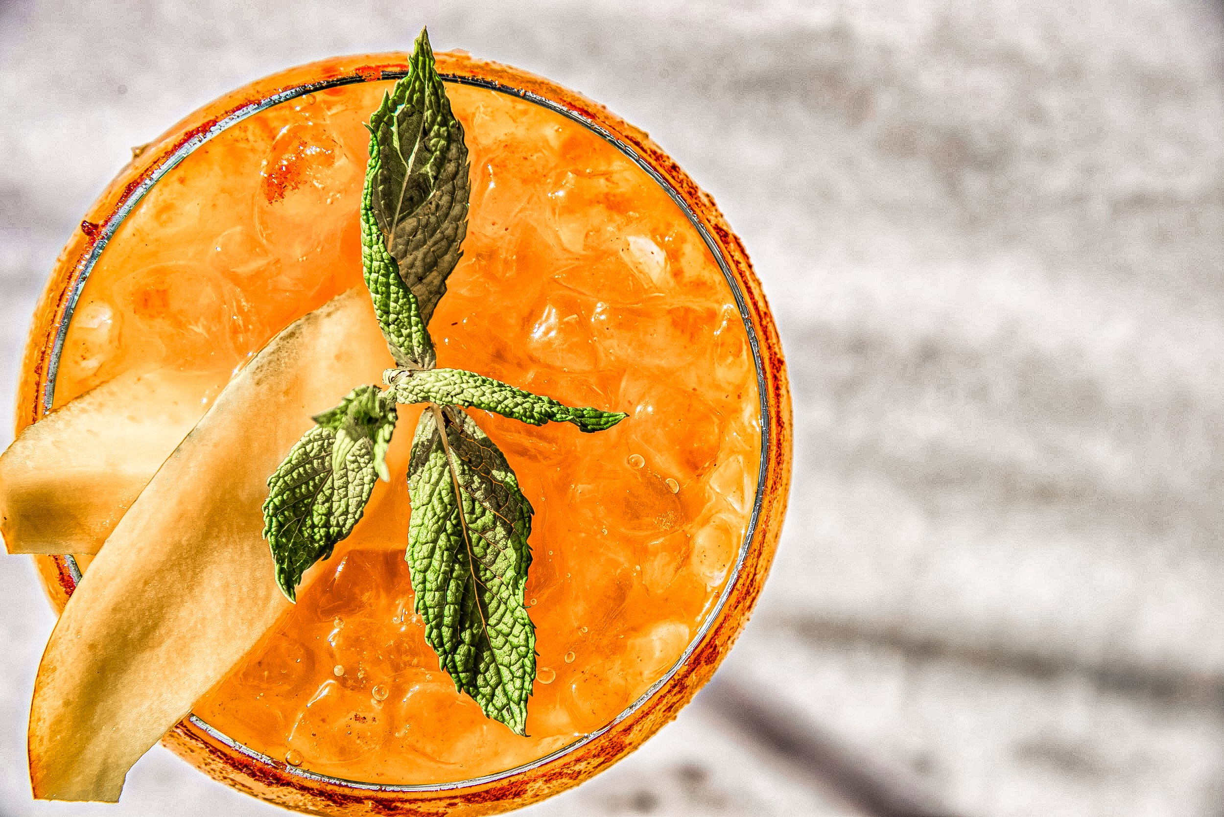 A top-down view of a glass filled with an orange-colored iced beverage garnished with fresh mint leaves and a slice of pear.