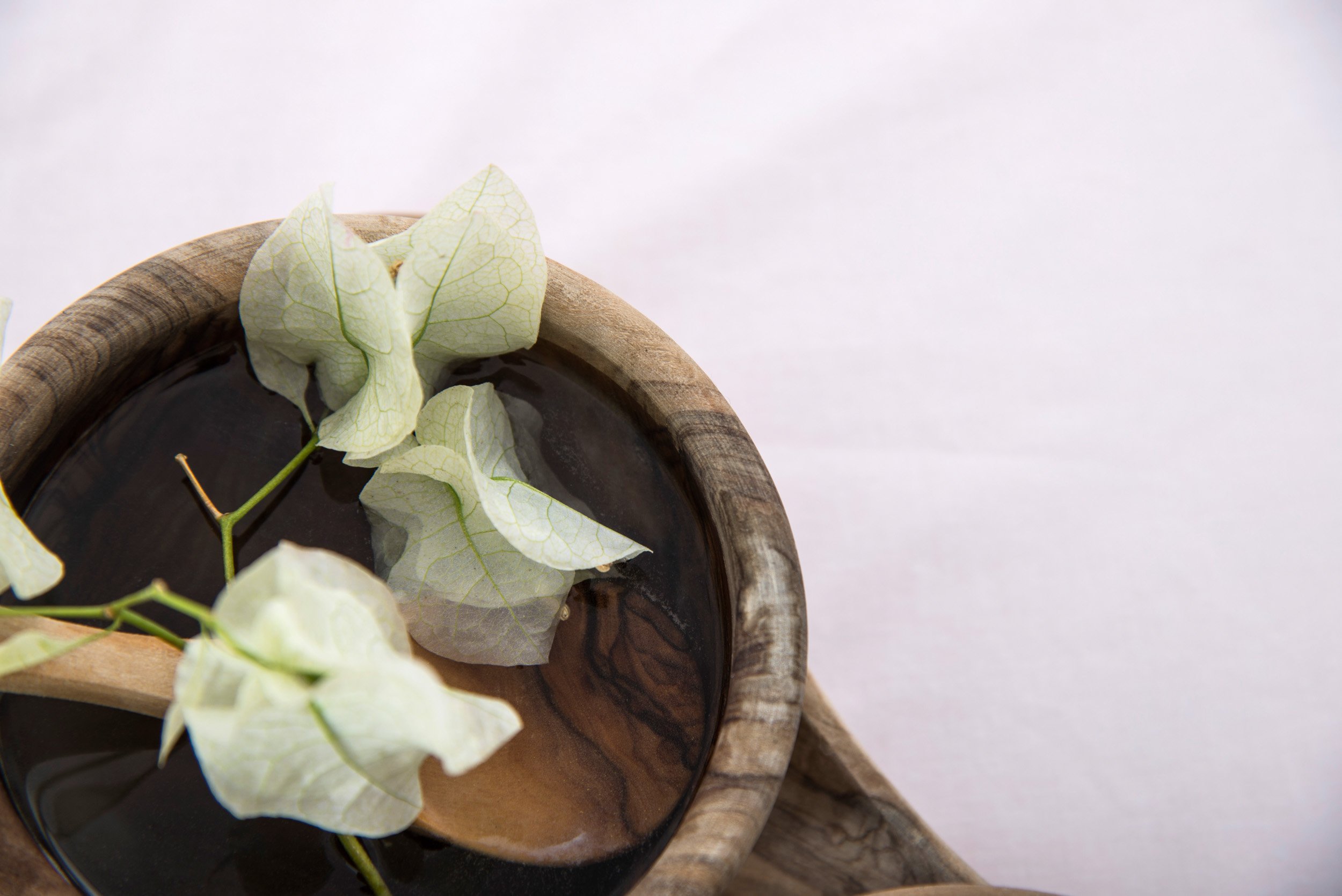 A wooden bowl filled with dark liquid and light green leaves floating on top, placed on a white surface.