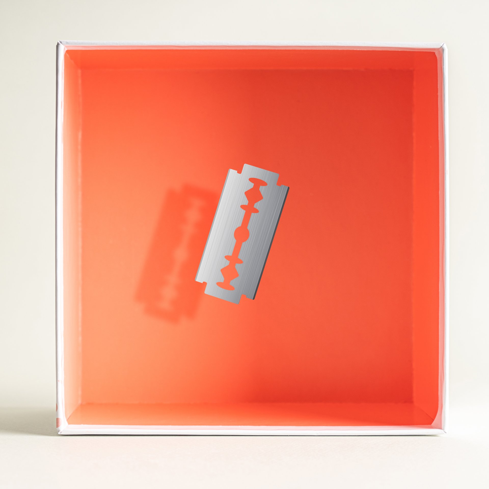 Inside of a white box with an orange interior, featuring a silver razor blade centered.