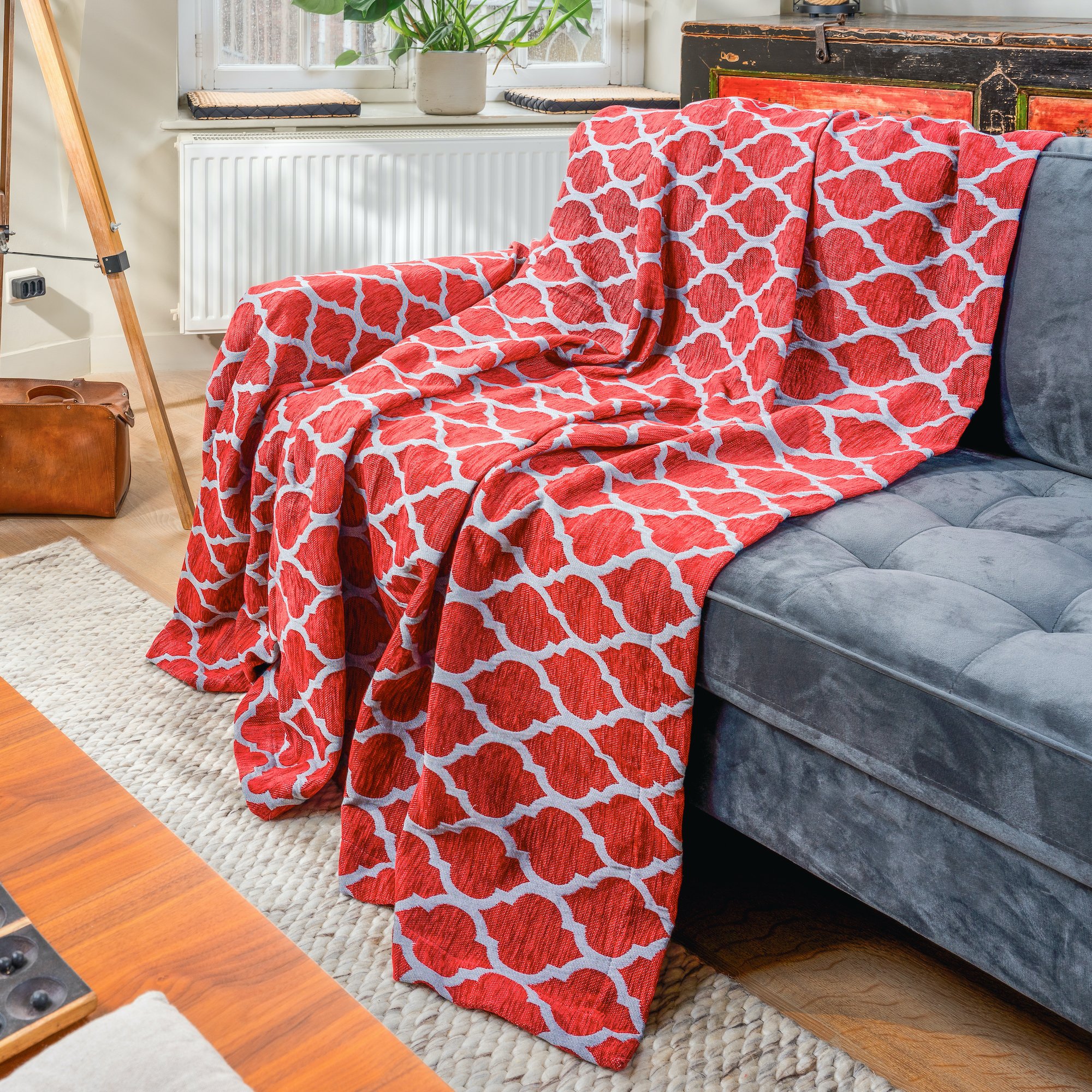 A gray velvet sofa with a red and white patterned throw blanket draped over it in a cozy living room.