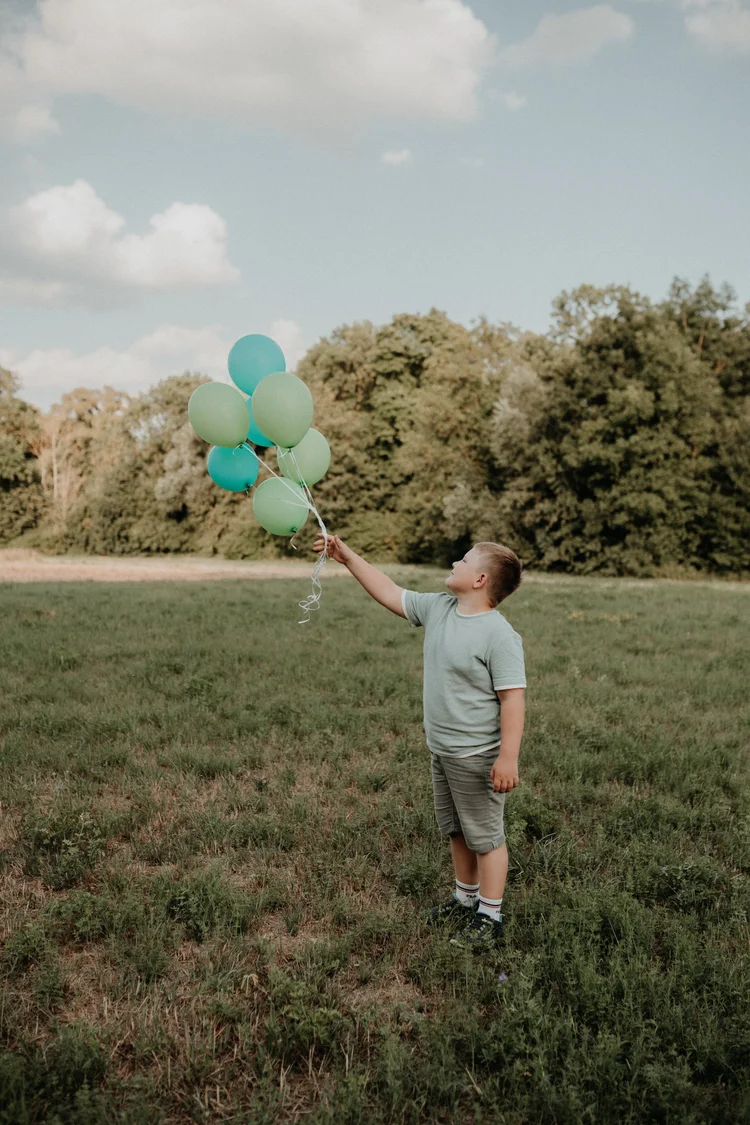 Junge hält einen Strauß Luftballons auf der Wiese