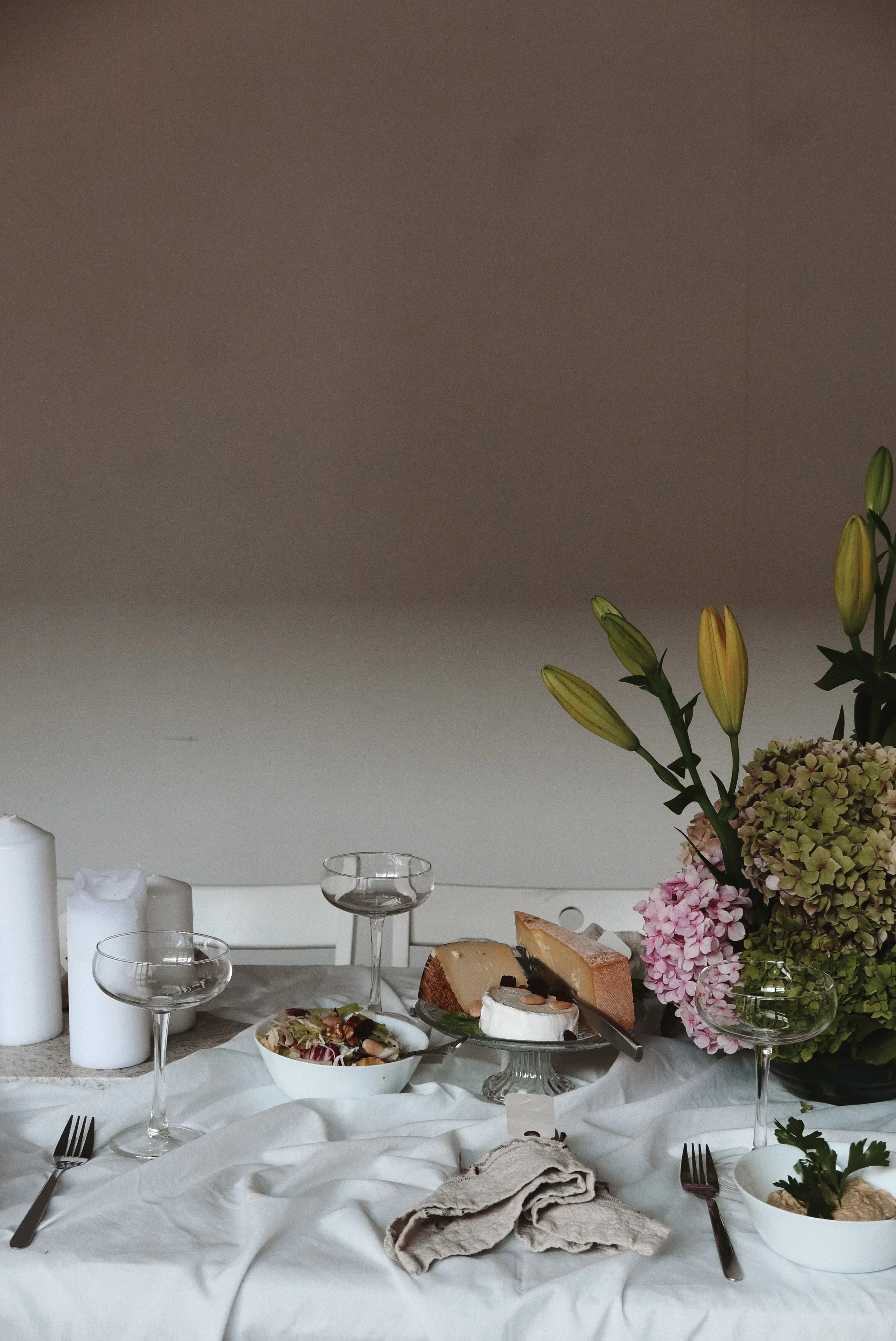 Table set with white tablecloth, candlesticks, two glasses, a bowl of salad, a half-eaten cake, flowers, and utensils.