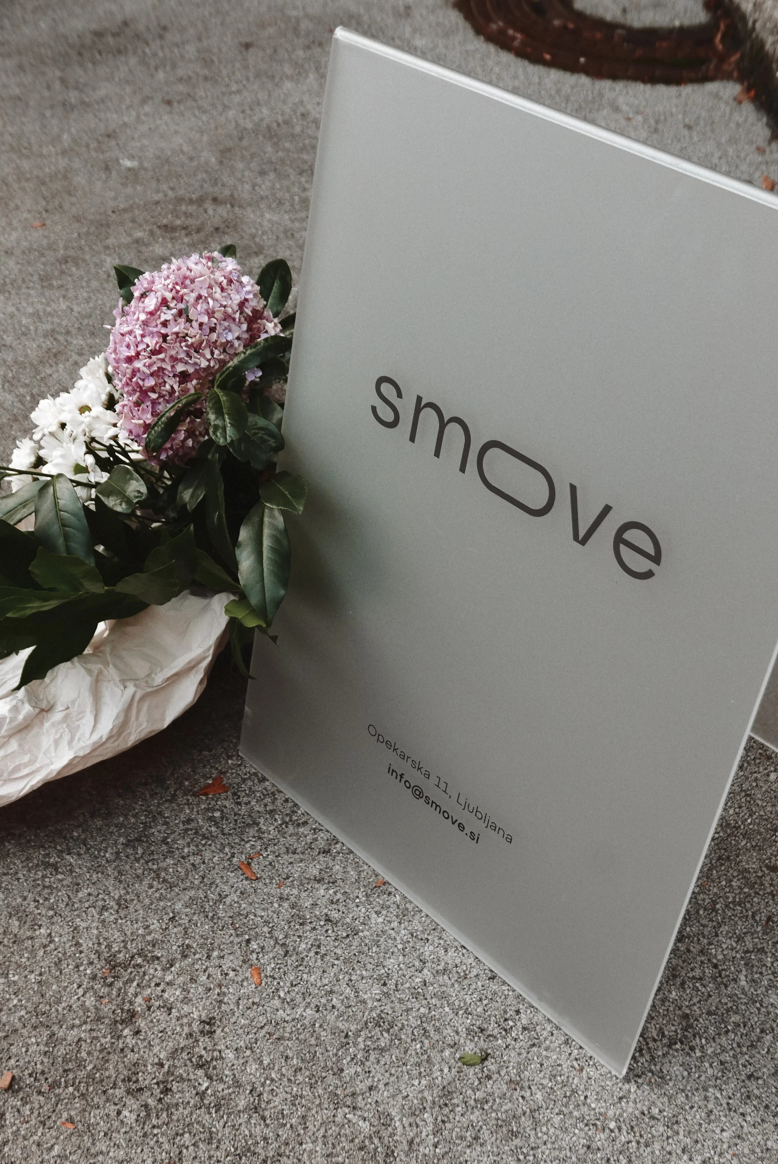A flower arrangement with pink and white flowers next to a gray sign that reads 'smove' with an address and contact information underneath.