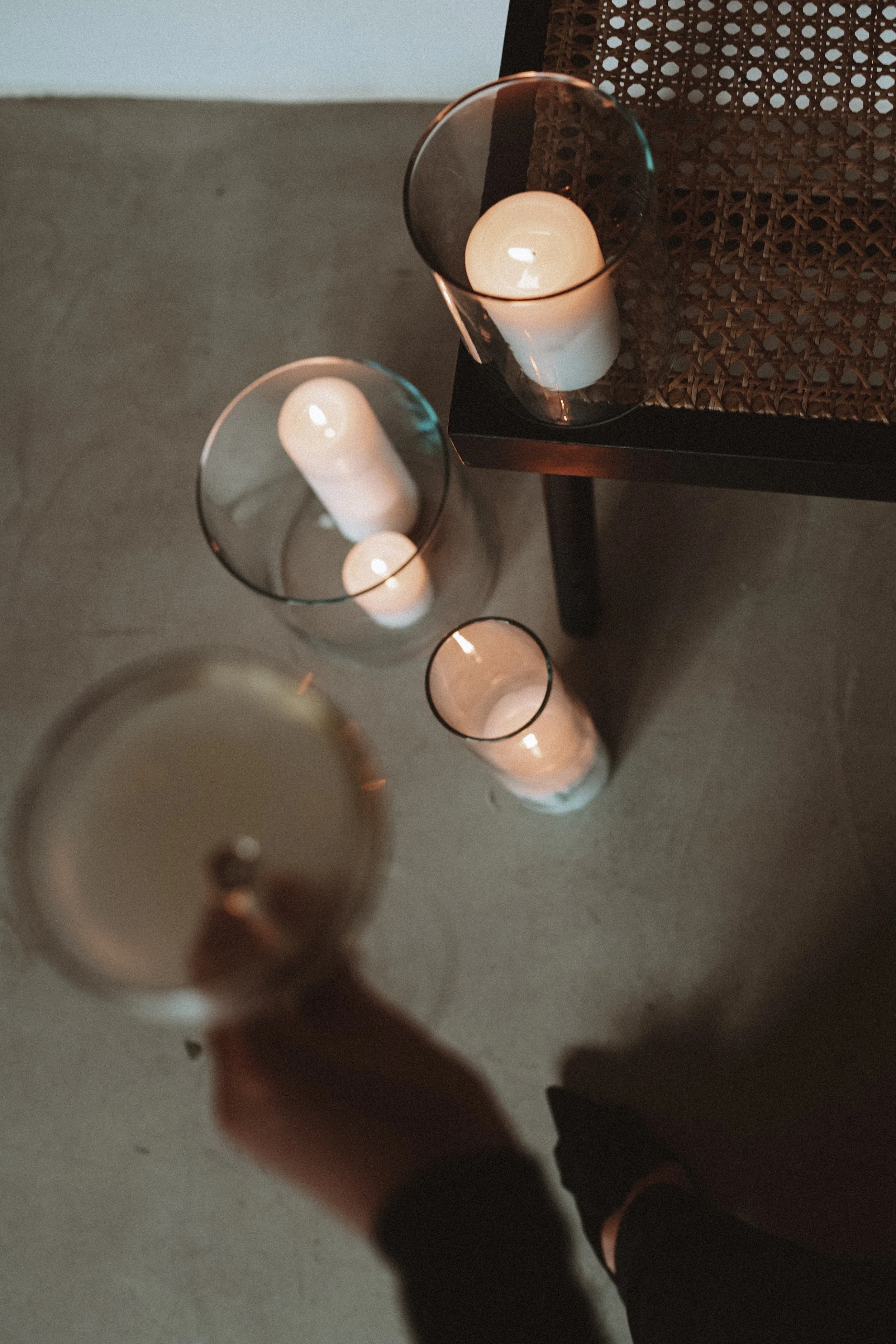 Top-down view of four candles in glass holders on a concrete floor near a woven chair.