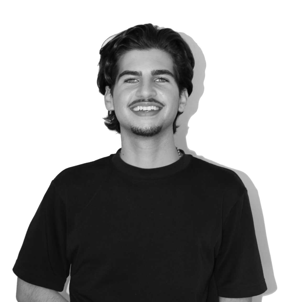 Black and white photo of a young man with dark hair, a goatee, and a mustache, smiling, wearing a black T-shirt.