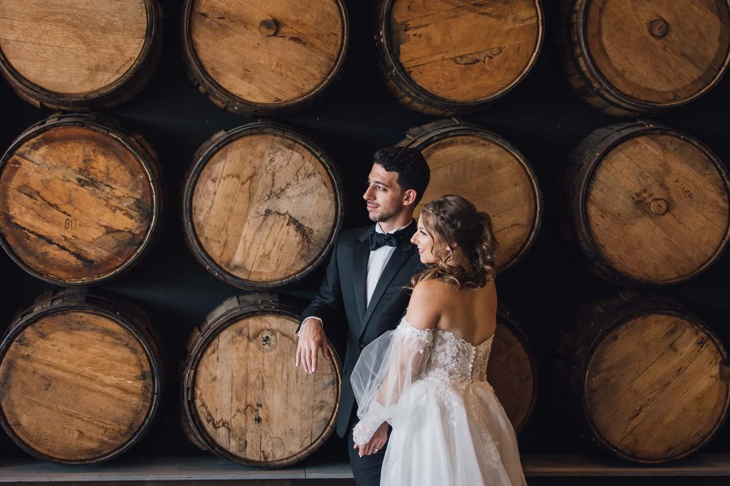A bride and groom smile and pose in front of rustic wooden barrels