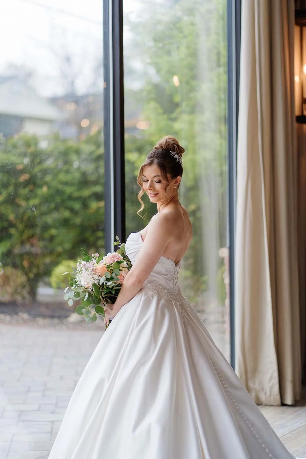 Close-up portrait of a bride looking down at her bouquet by the massive glass windows of the Farmview Room.