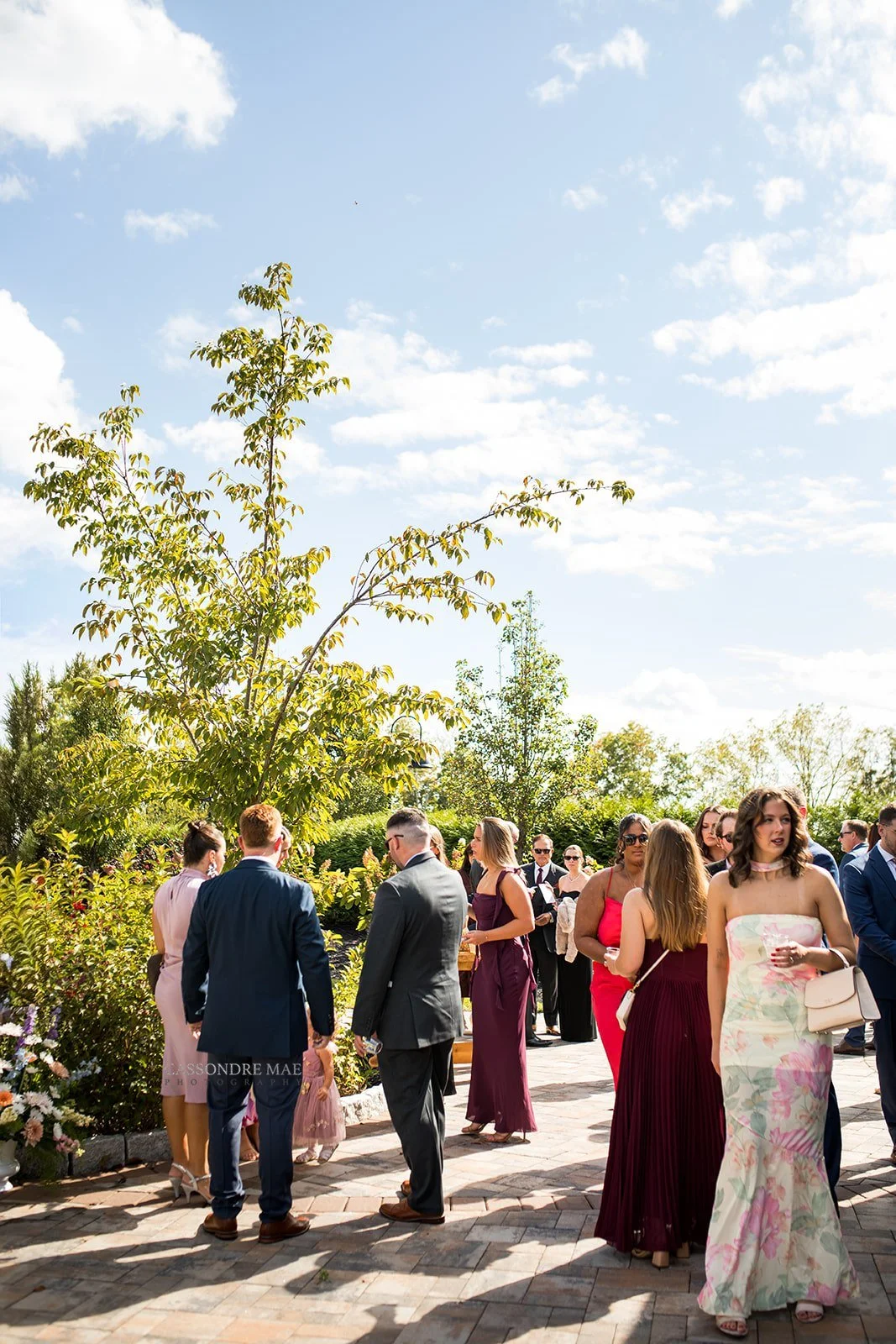 Wedding guests mingling on a sun-drenched outdoor paved patio during cocktail hour at a wedding venue in upstate NY