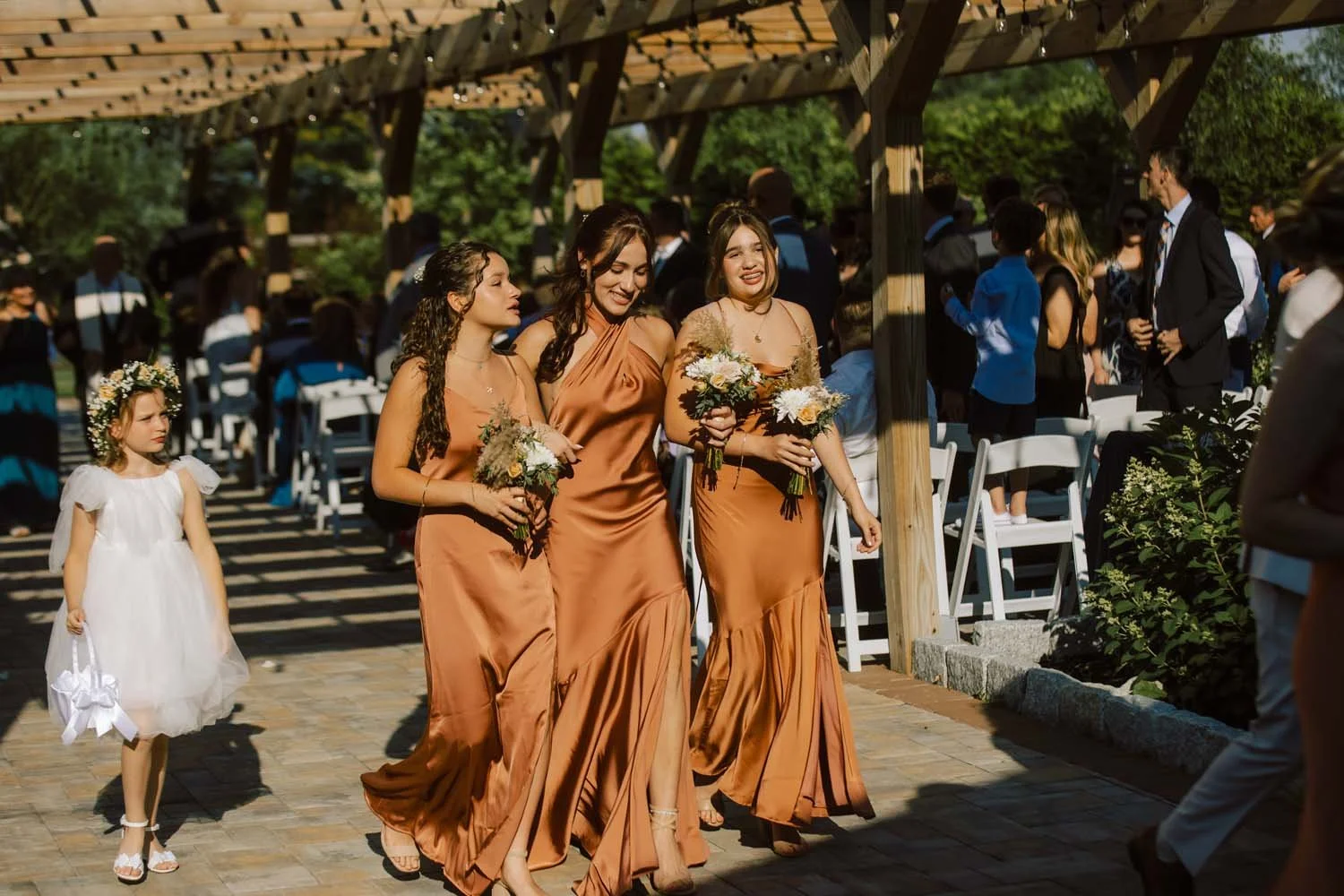 Bridesmaids in copper satin dresses walking under the pergola at a cozy outdoor barn wedding in NY