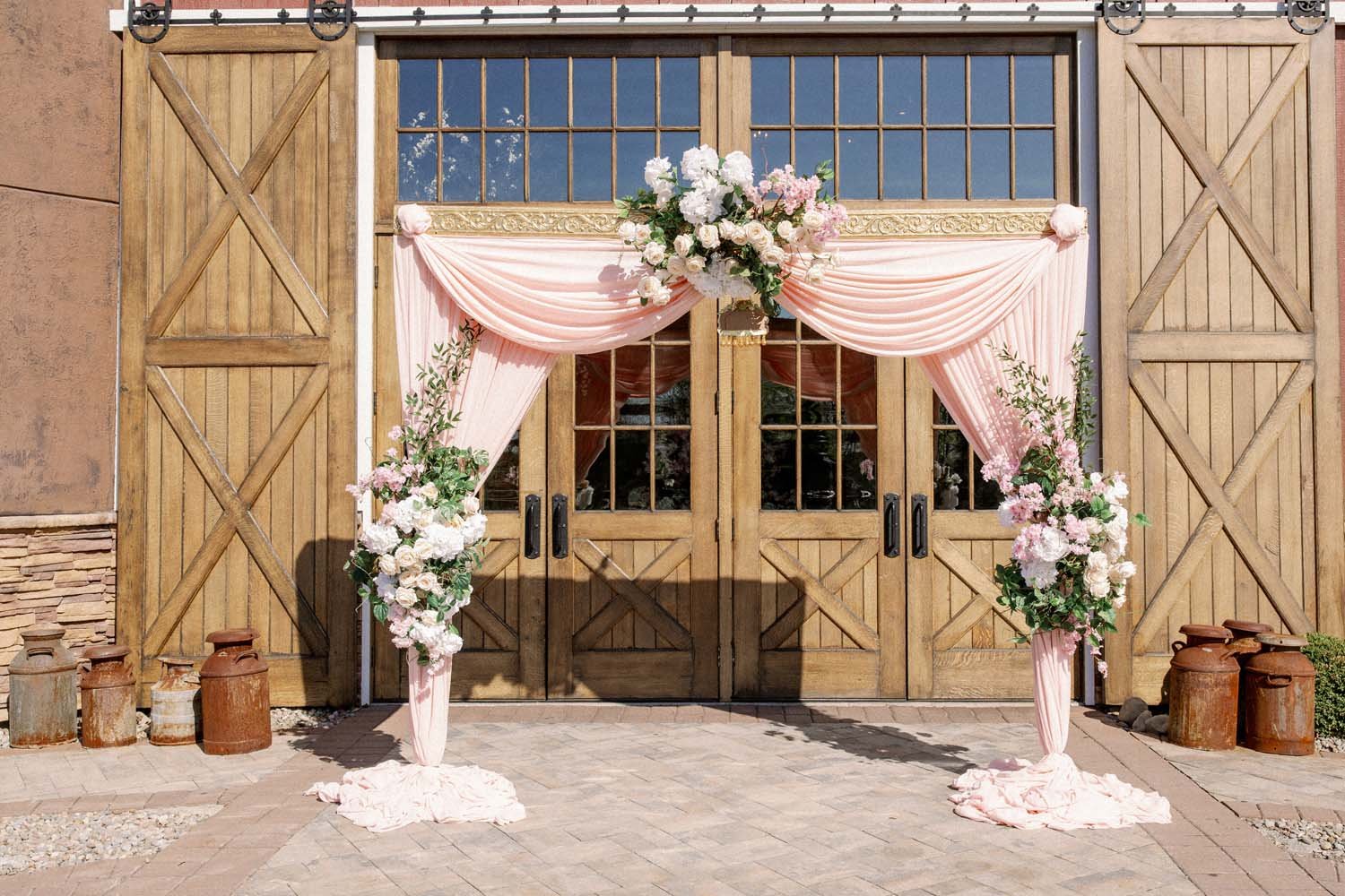 An arch with flowers and soft pink drapery sits in front of the gorgeous wooden barn doors.