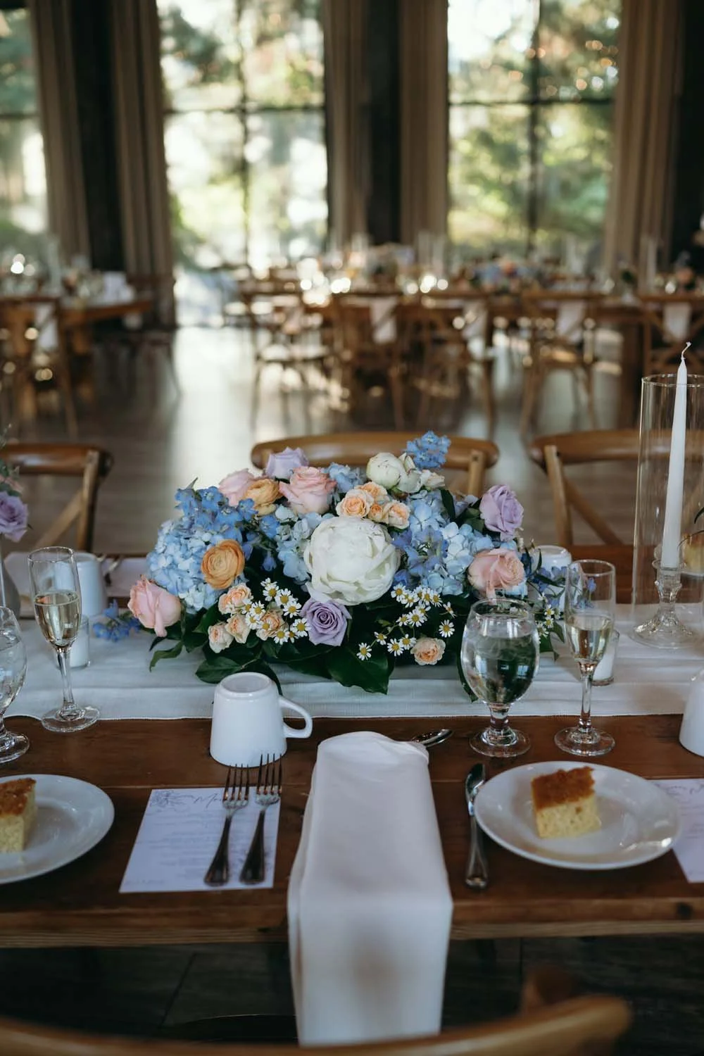 Farm table reception setup featuring baby blue and pastel floral centerpiece with taper candles