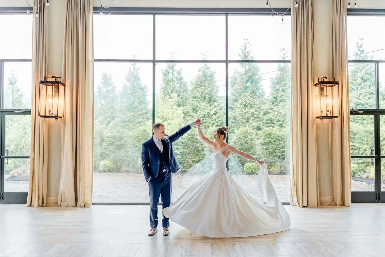 Groom twirling bride in front of floor-to-ceiling windows inside the Farmview Room at The Barn at Villa Venezia.