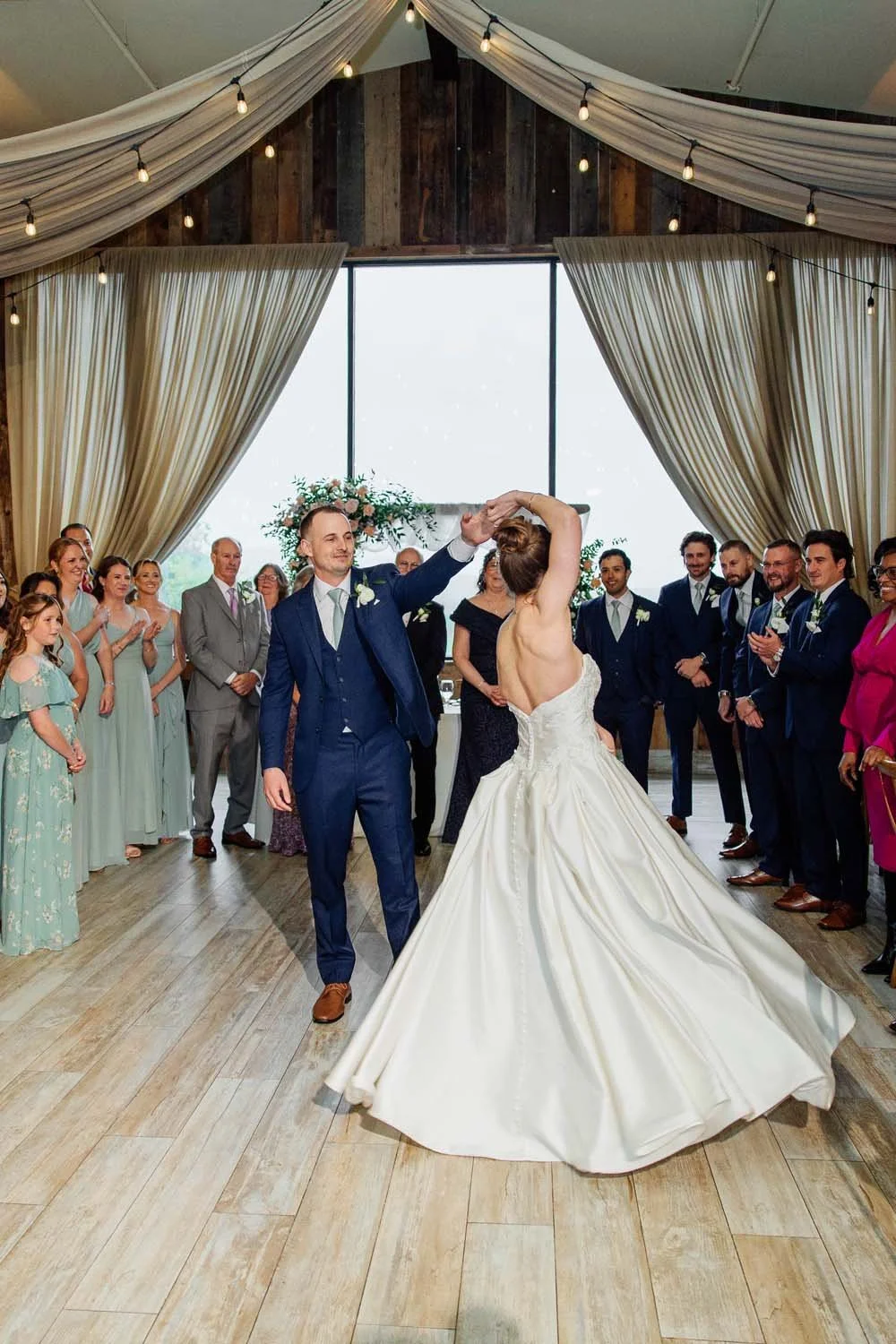 Bride and groom sharing their first dance on the polished floors of the Farmview Room surrounded by wedding guests.