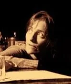 Person lying on a table with a paper and a glass in front, illuminated by warm light.