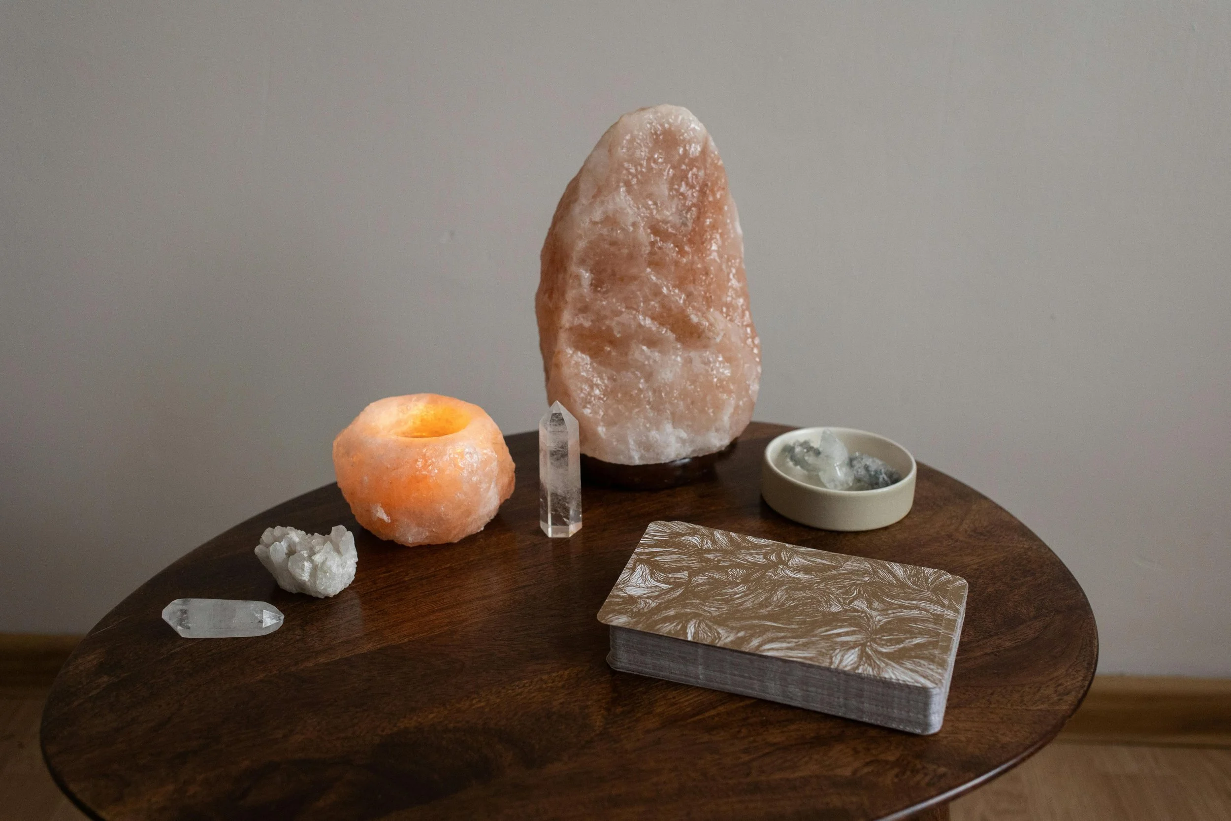 A collection of salt lamps, crystals, and tarot cards on a wooden table.
