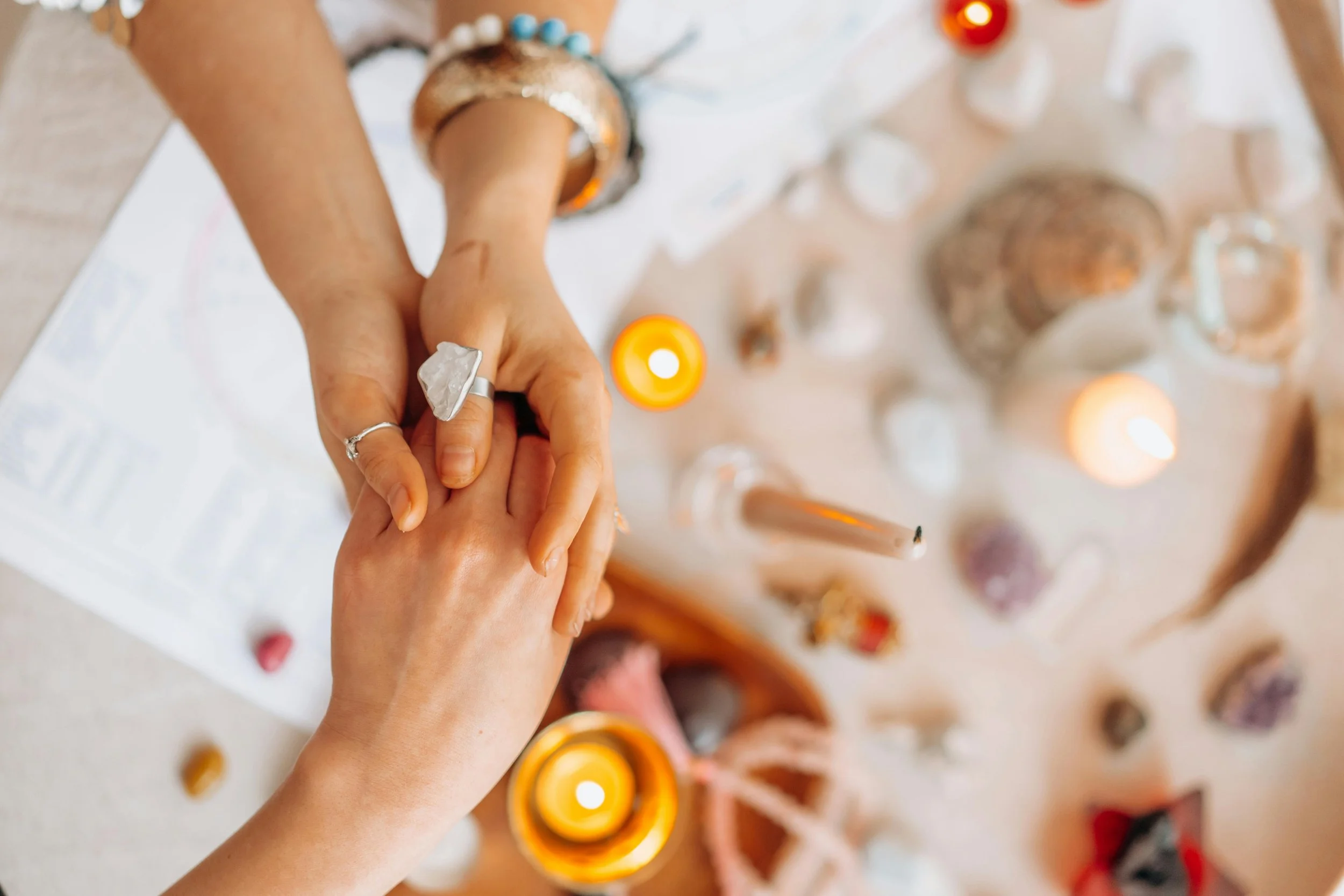 Hands holding each other over a surface with candles and crystals.