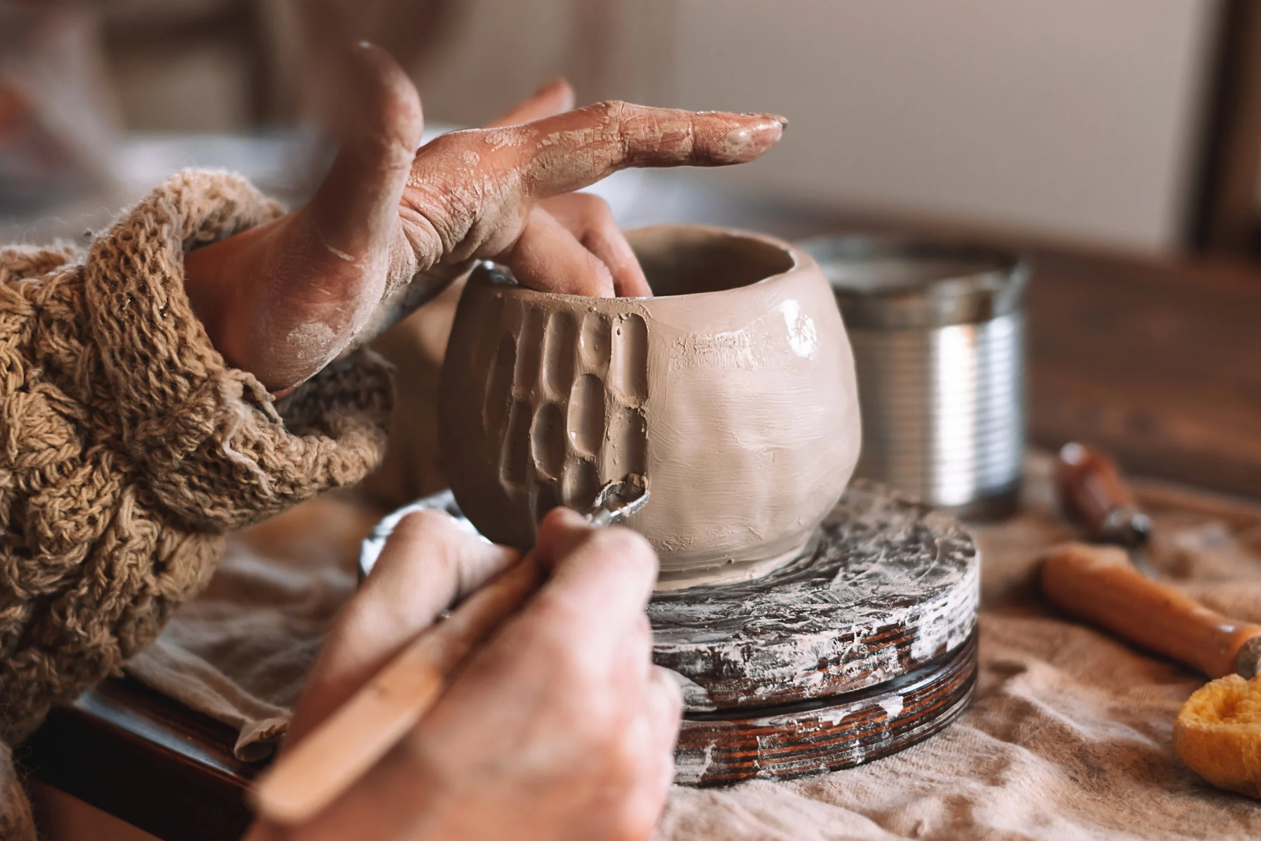 A person shaping a ceramic mug on a pottery wheel in a pottery studio.