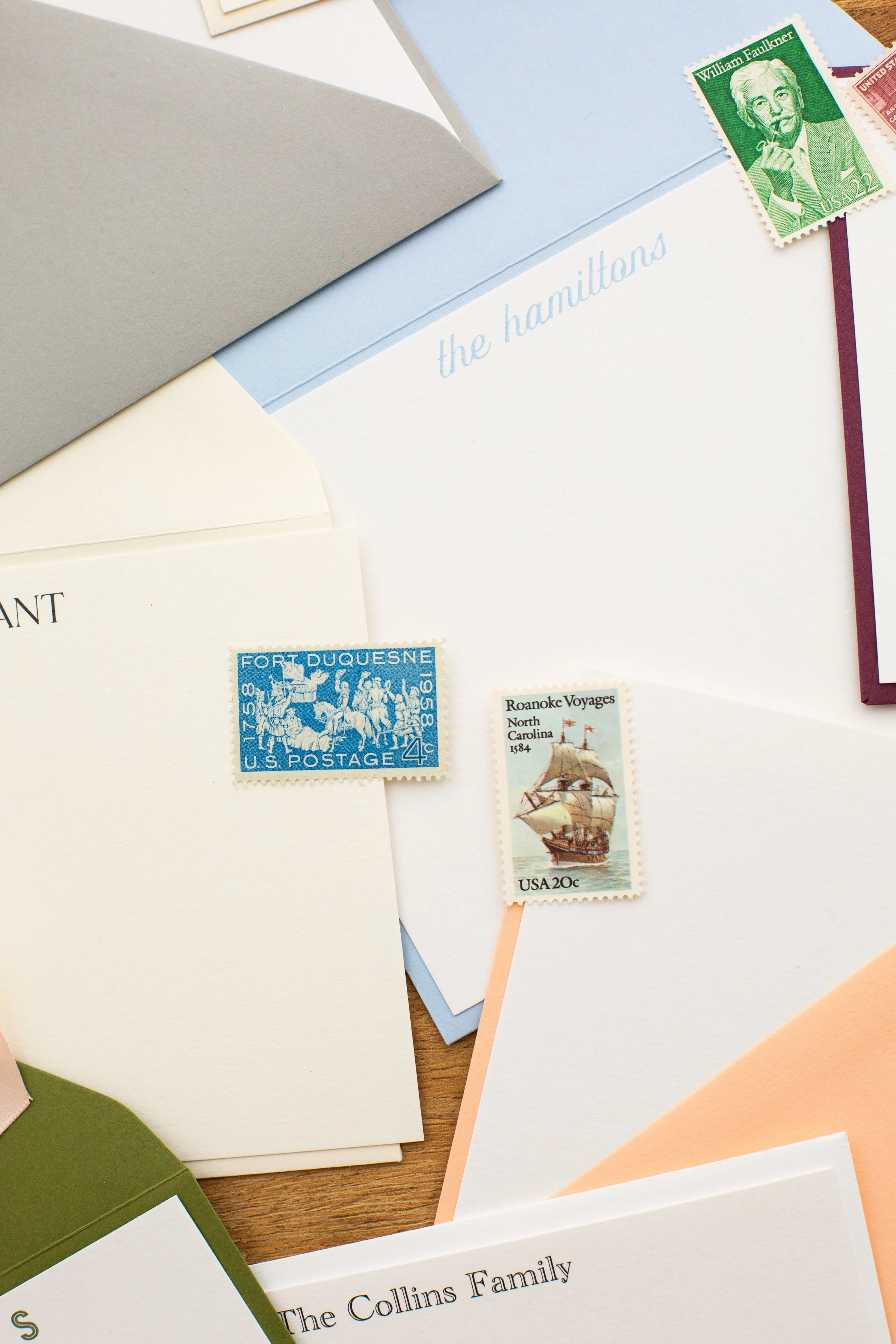 Flat lay of personalized stationery and envelopes in soft, muted tones with vintage stamps, featuring names including “The Hamiltons” and “The Collins Family.”
