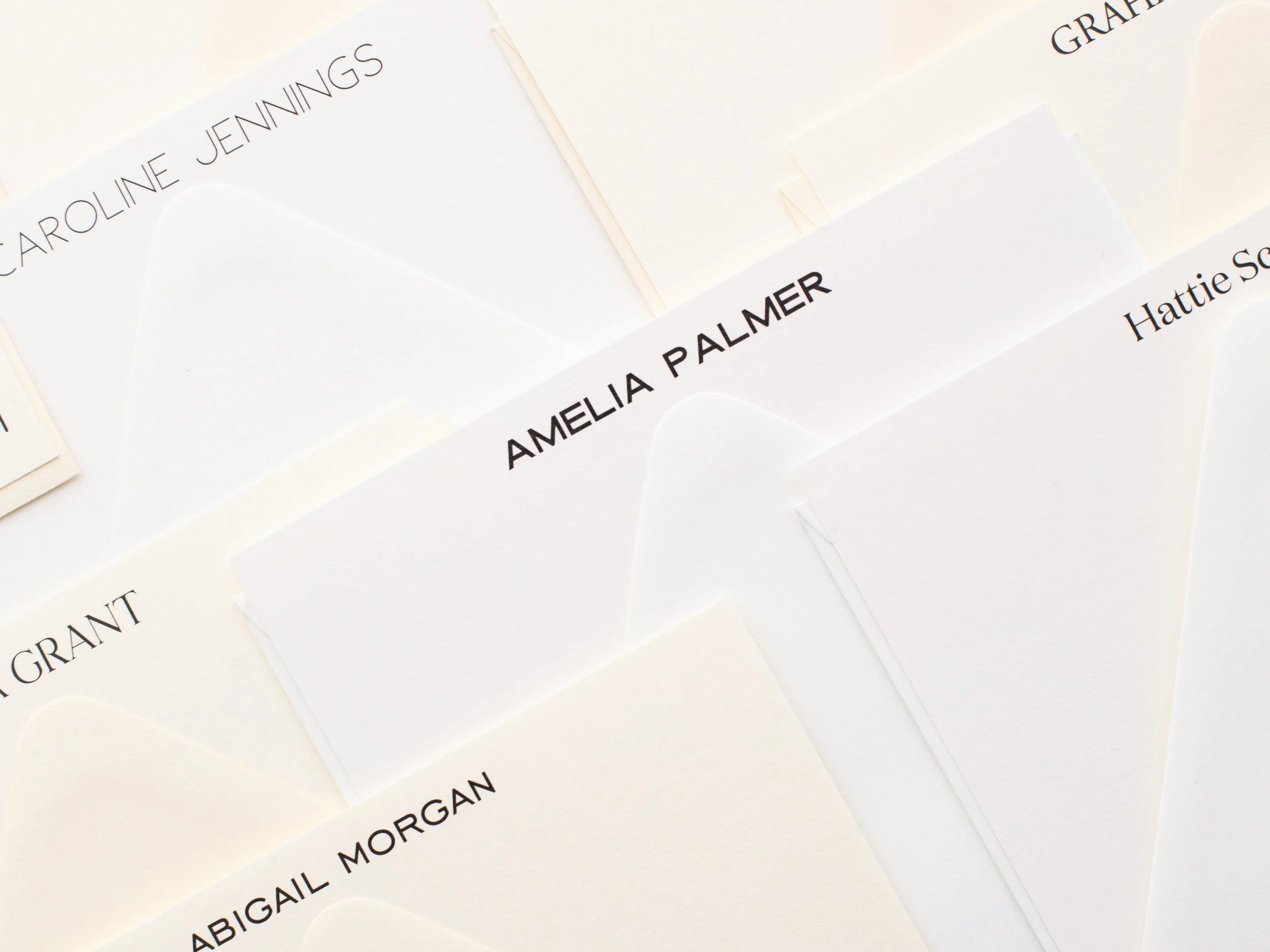 Close-up of neutral-toned personalized stationery and envelopes featuring names including “Amelia Palmer,” “Caroline Jennings,” and “Abigail Morgan.”