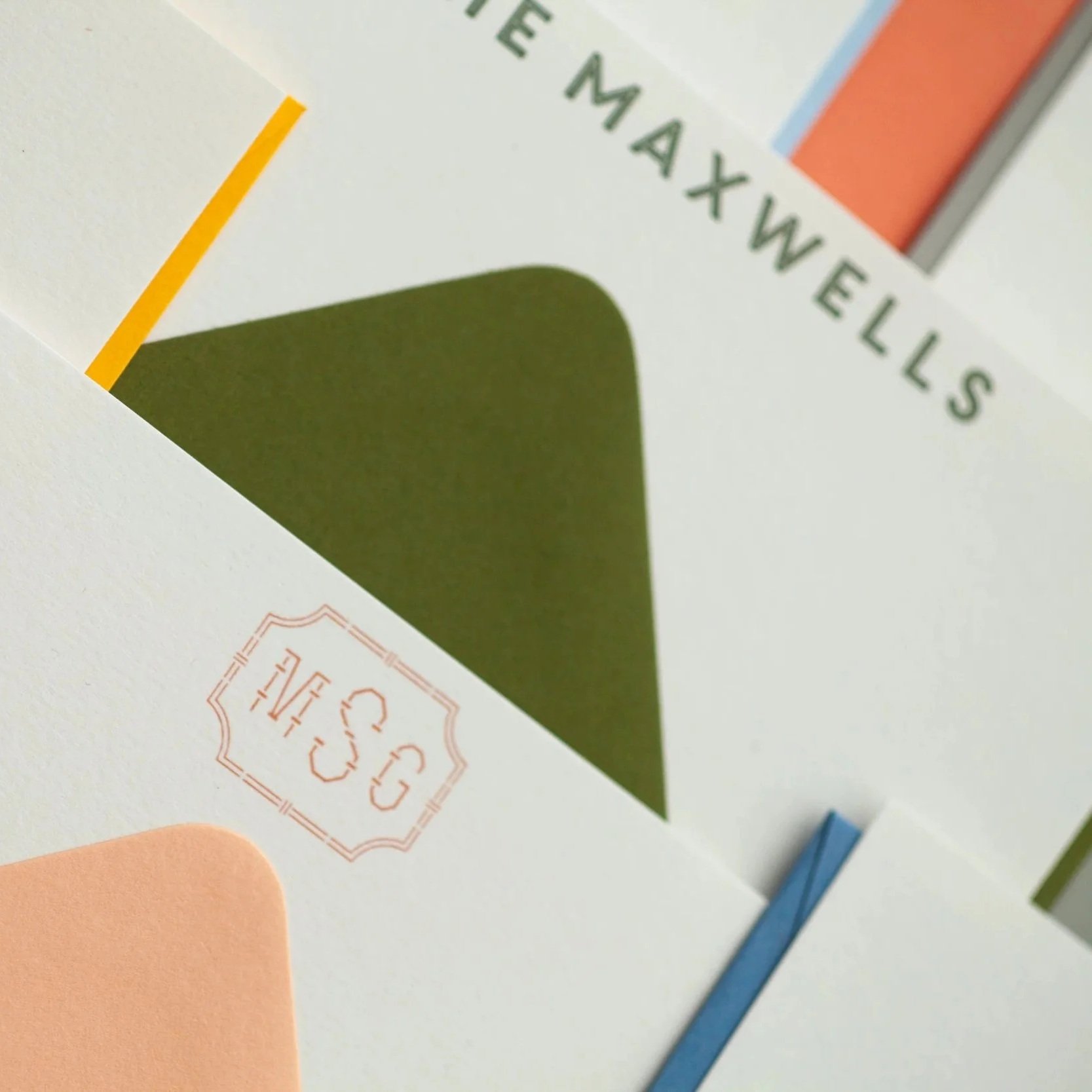 Close-up of personalized stationery cards with colorful geometric designs, featuring a monogram and the name “The Maxwells.”