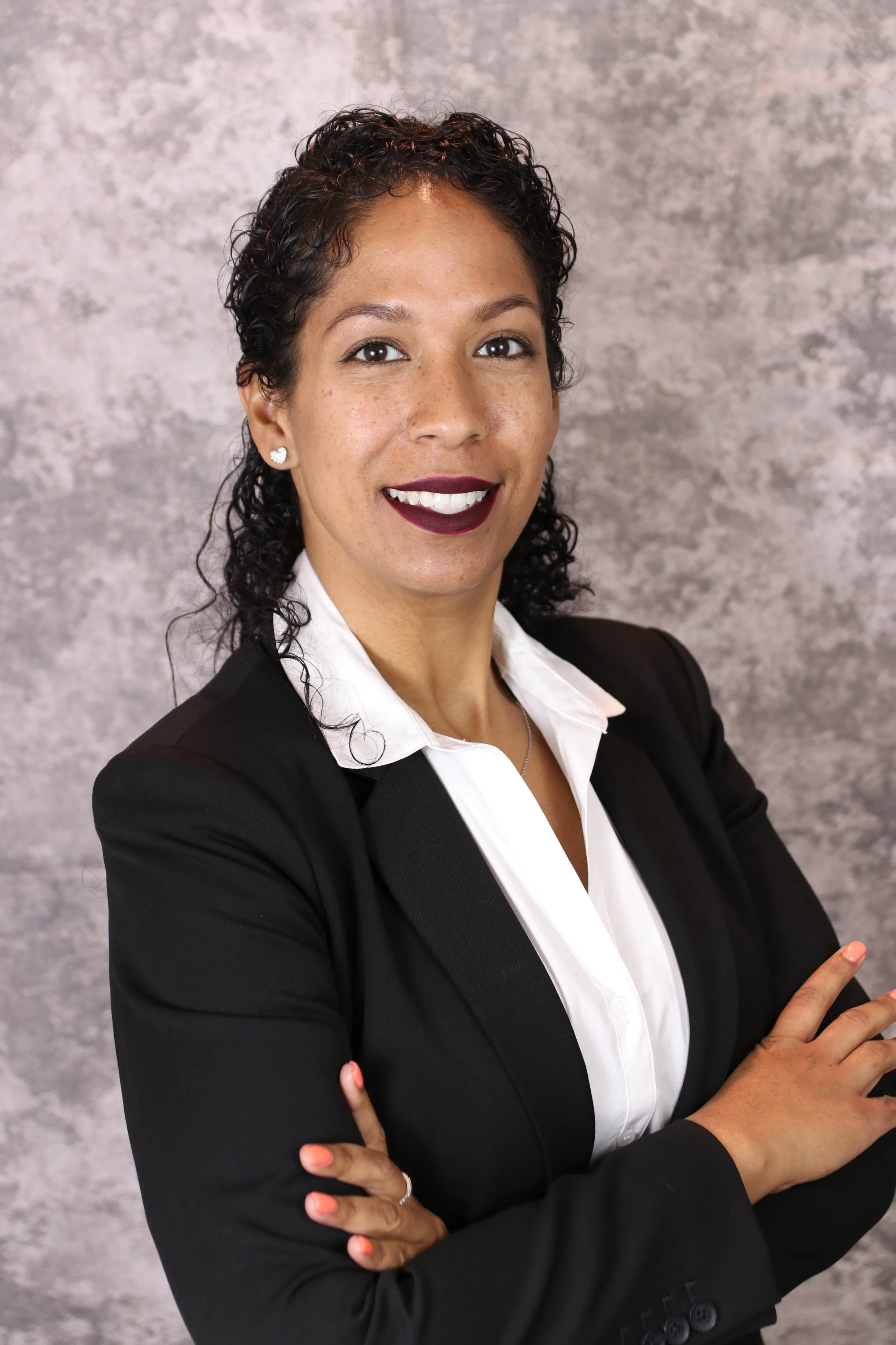 "Karina Orfilia, founder of Purple Royalty LLC, smiling confidently in a black blazer and white blouse—professional branding photo with gray studio background."