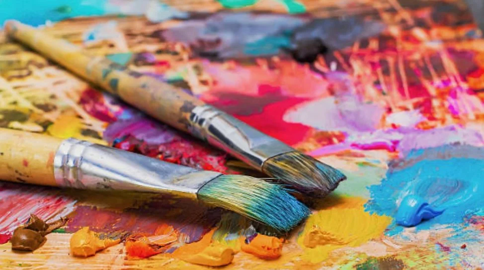 Paintbrushes resting on a palette full of colourful paint colours