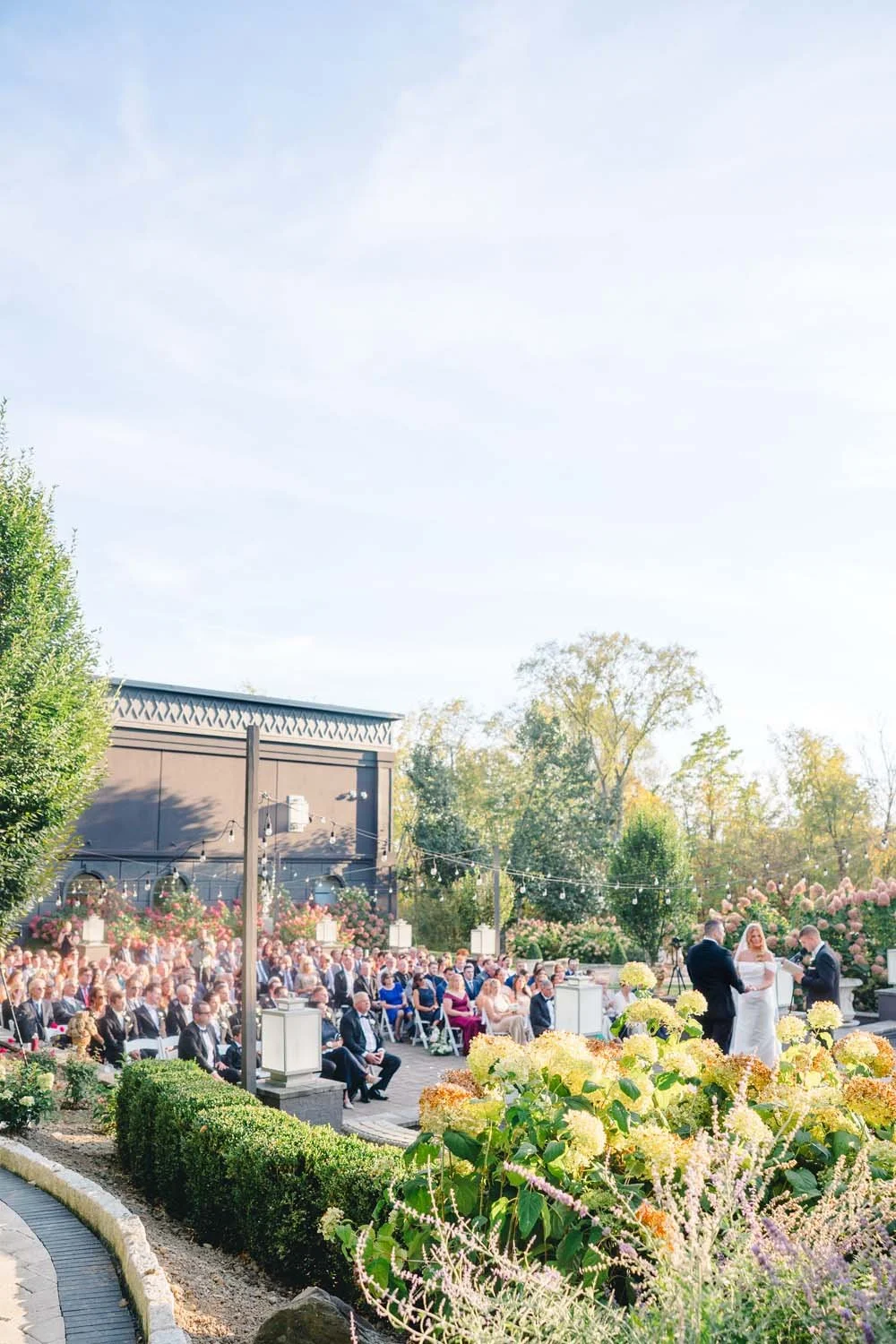 Outdoor wedding ceremony at Villa Venezia with guests seated on a stone courtyard surrounded by blooming hydrangea bushes.