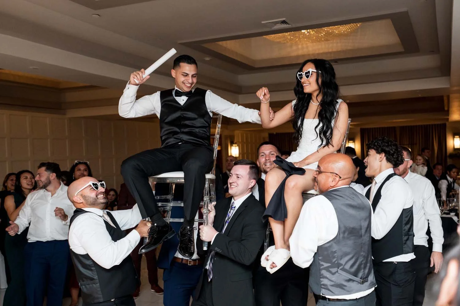 Bride and groom being lifted on chairs by guests during a high-energy wedding reception inside the Villa Venezia ballroom.