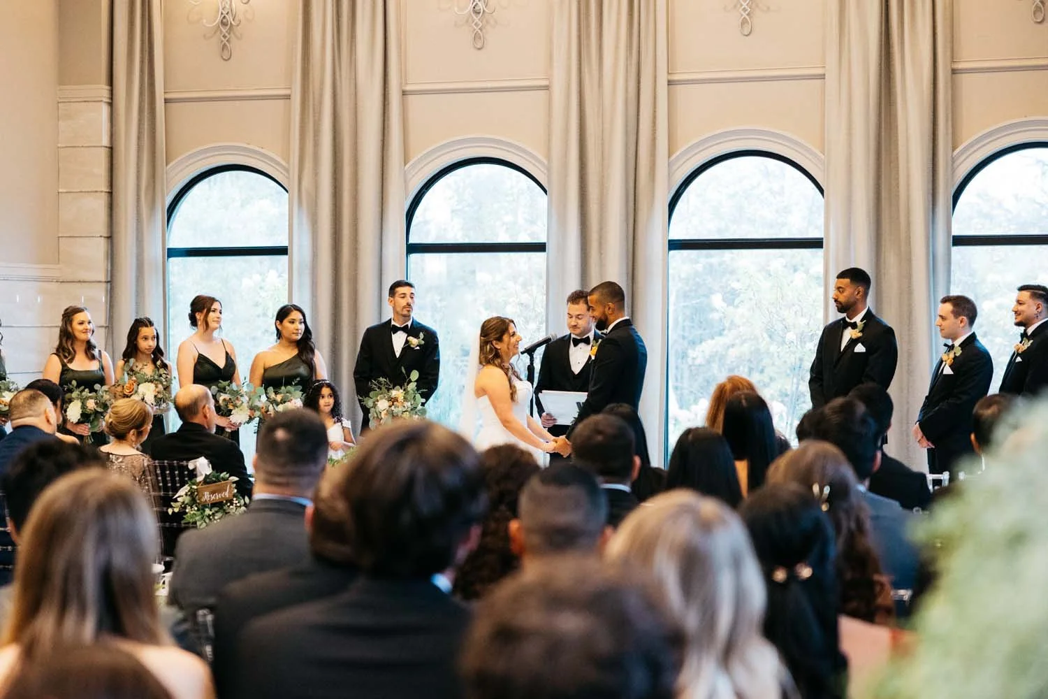 An elegant reception sweetheart table styled with a floral arch, romantic fairy lights, and candles on a reflective white ballroom floor