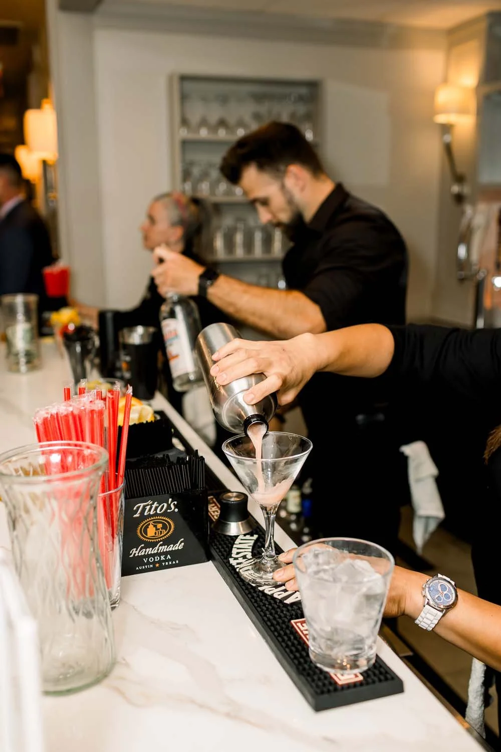 A professional bartender pouring a pink signature cocktail into a martini glass at Villa Venezia.