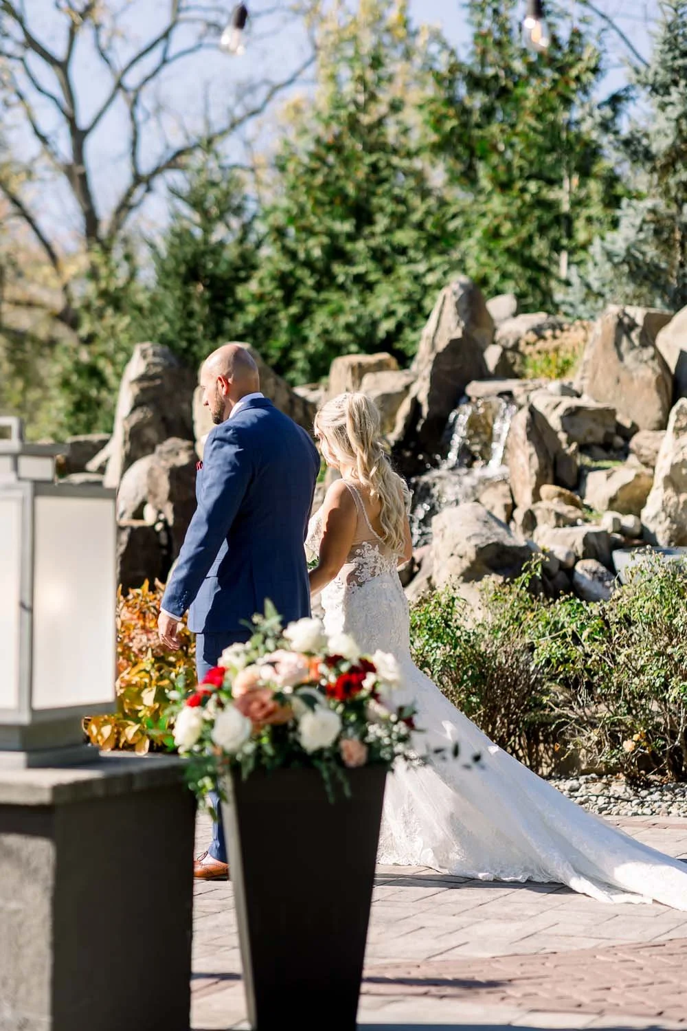 Bride and groom walking past a stone waterfall altar with red and white wedding florals at Villa Venezia.
