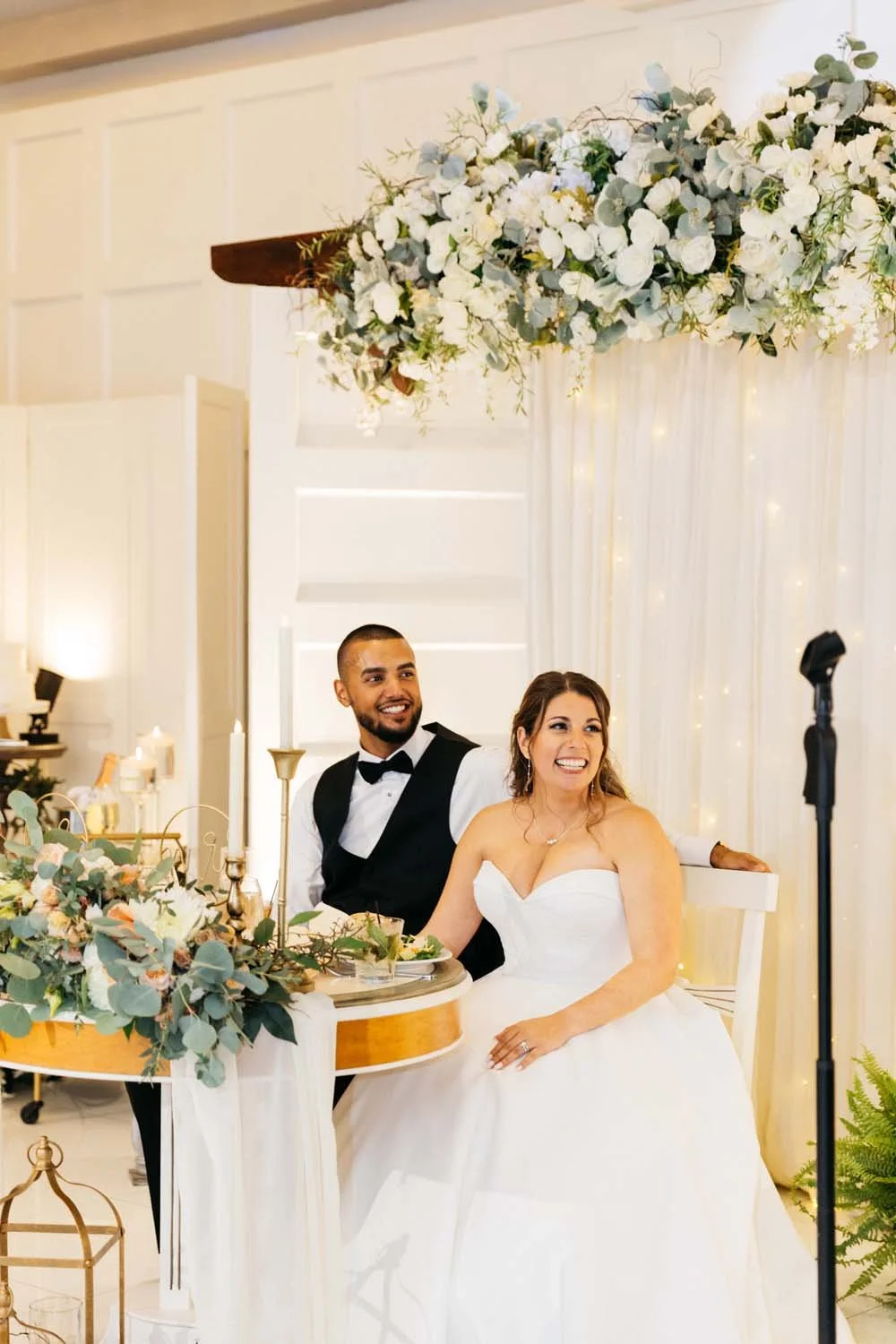Newlyweds smiling happily together at their beautifully decorated sweetheart table inside the Villa Venezia ballroom