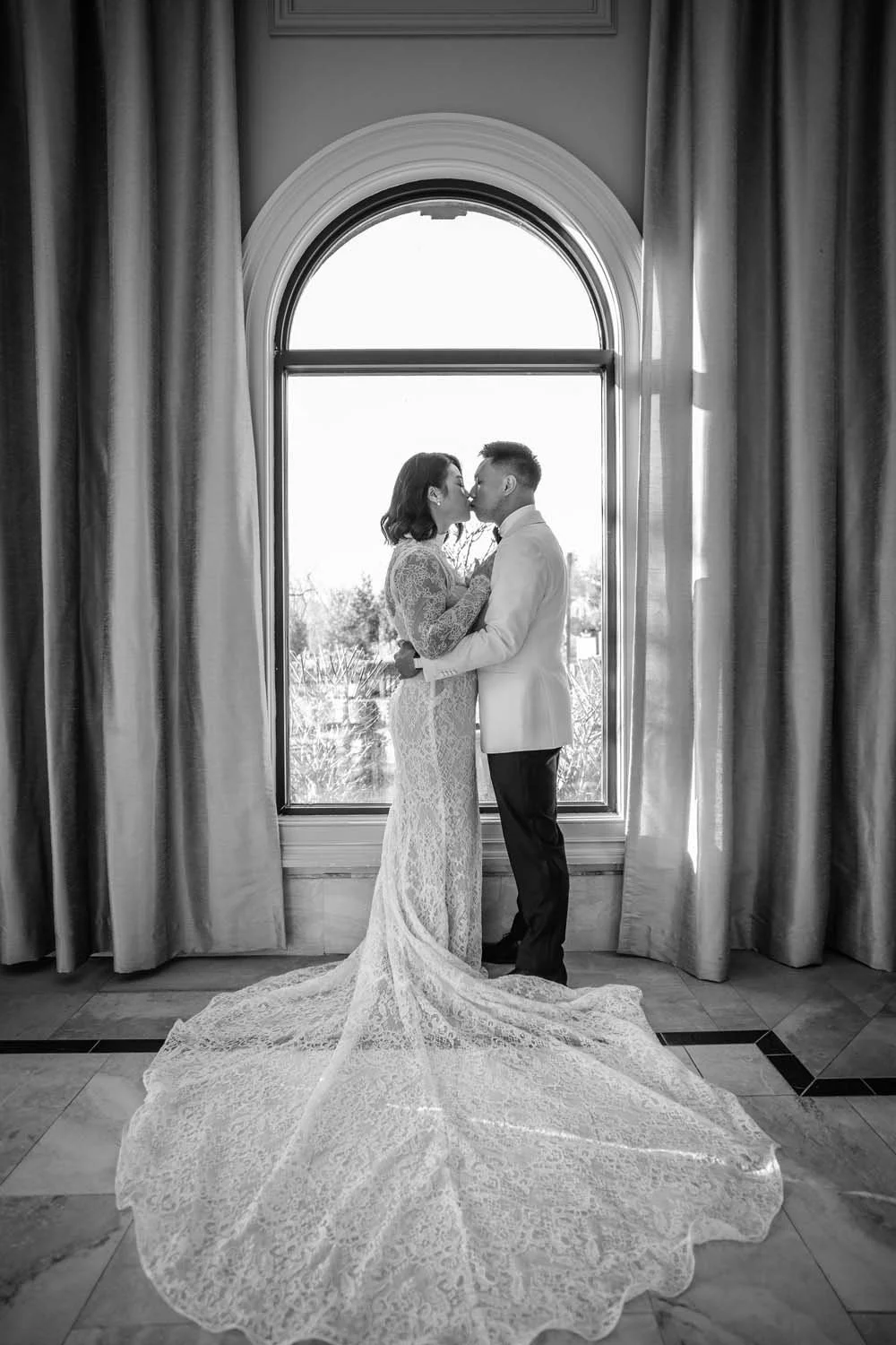A bride and groom stand in front of a large arched window at Villa Venezia in Hudson Valley