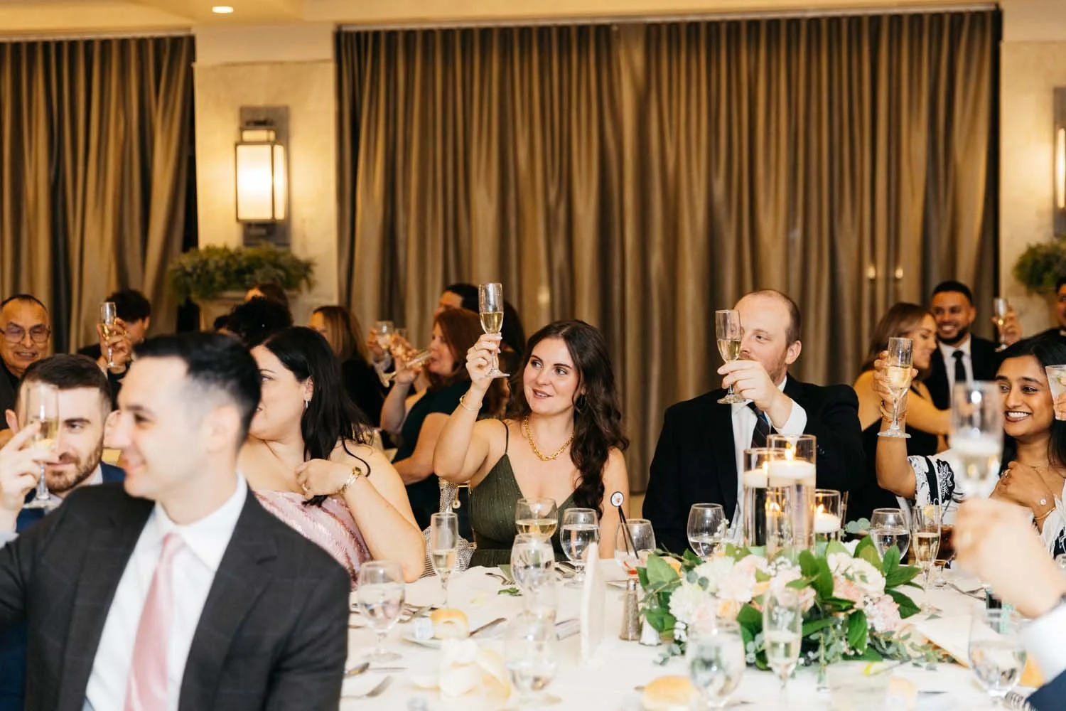 Wedding guests raising champagne glasses for a celebratory toast at a reception table inside a luxury Hudson Valley wedding venue