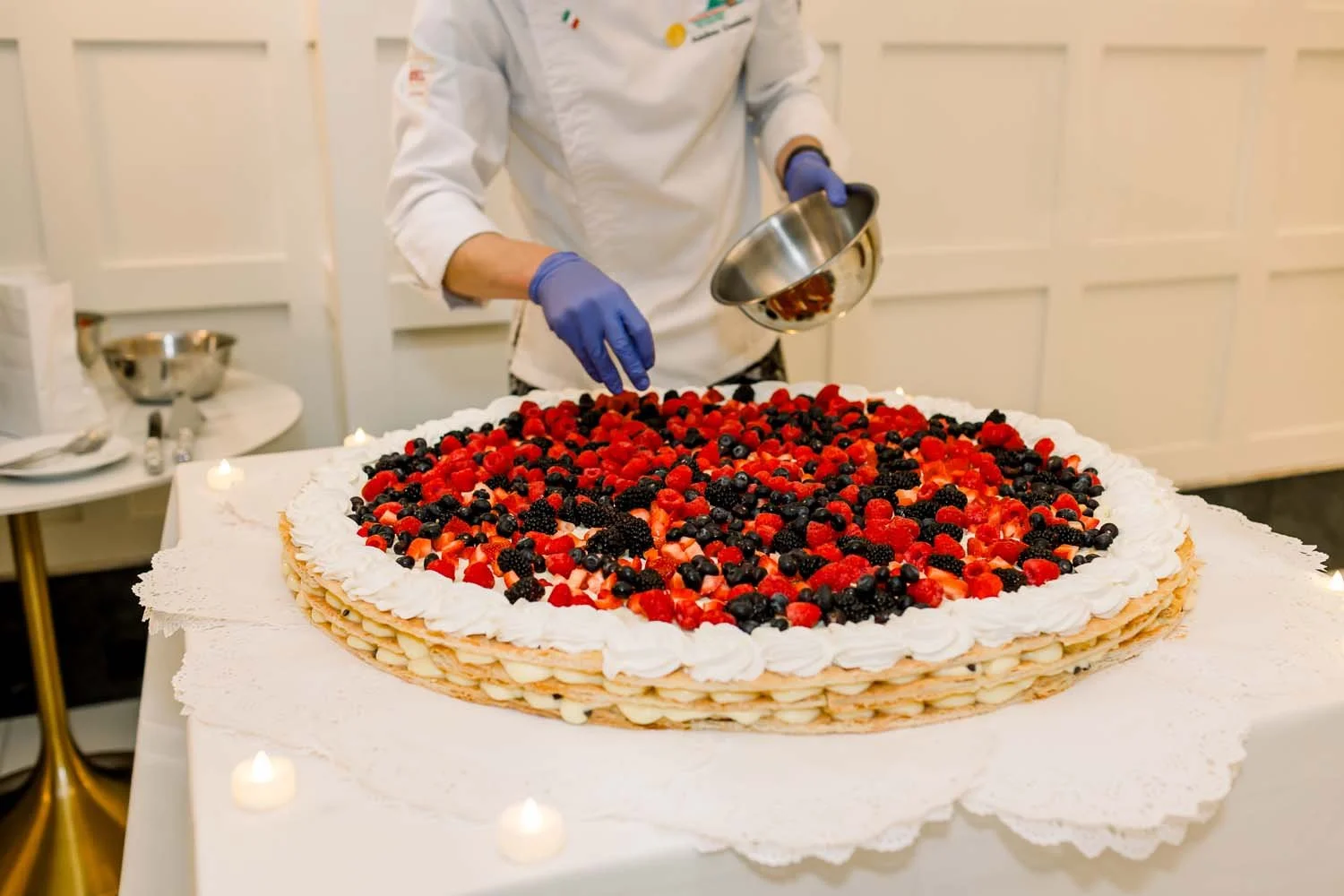 A professional chef assembling a massive traditional Italian millefoglie wedding cake with fresh berries for a reception.