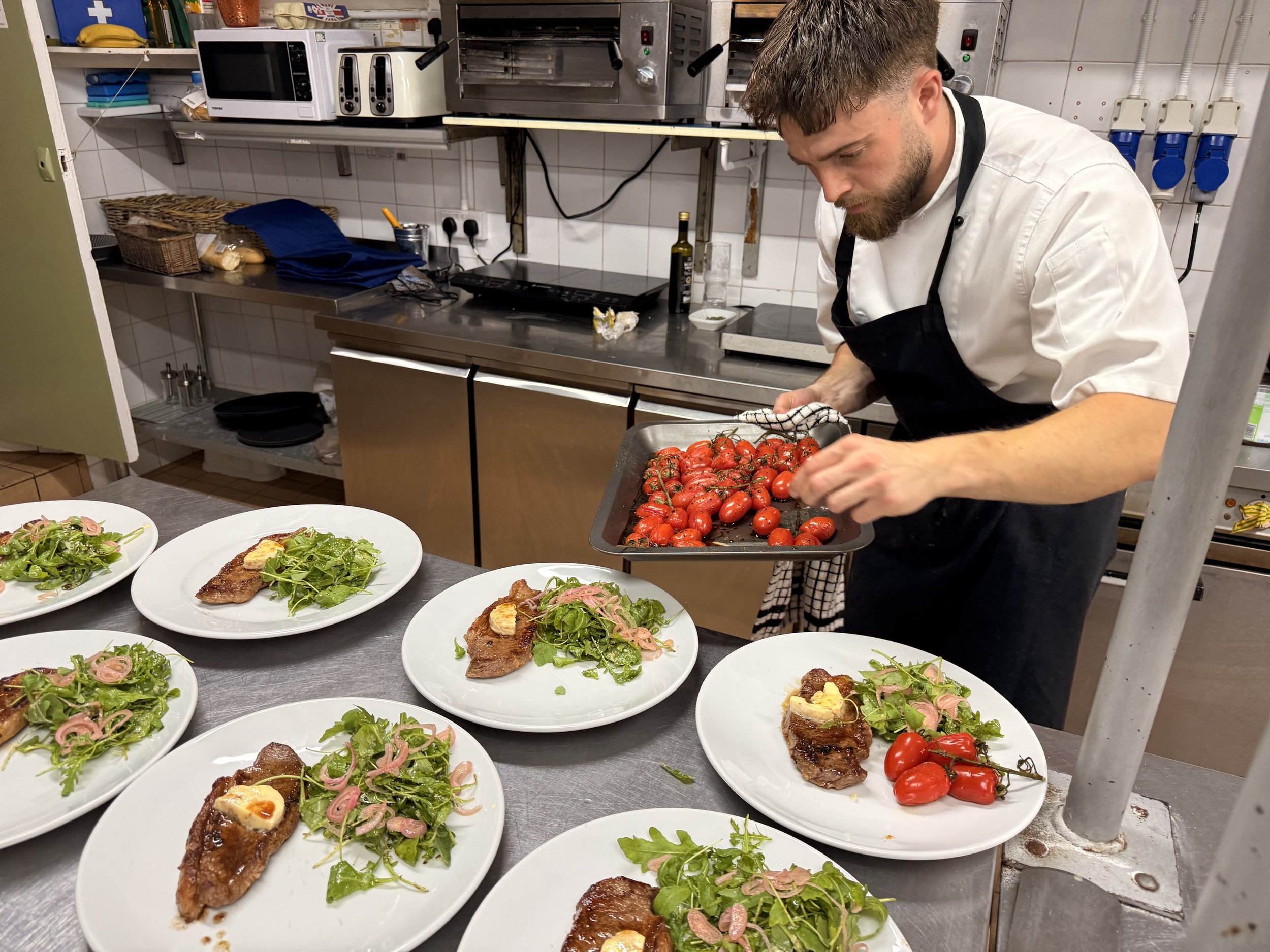 A chef preparing cherry tomatoes in a professional kitchen as multiple plates of plated food are ready on the counter.