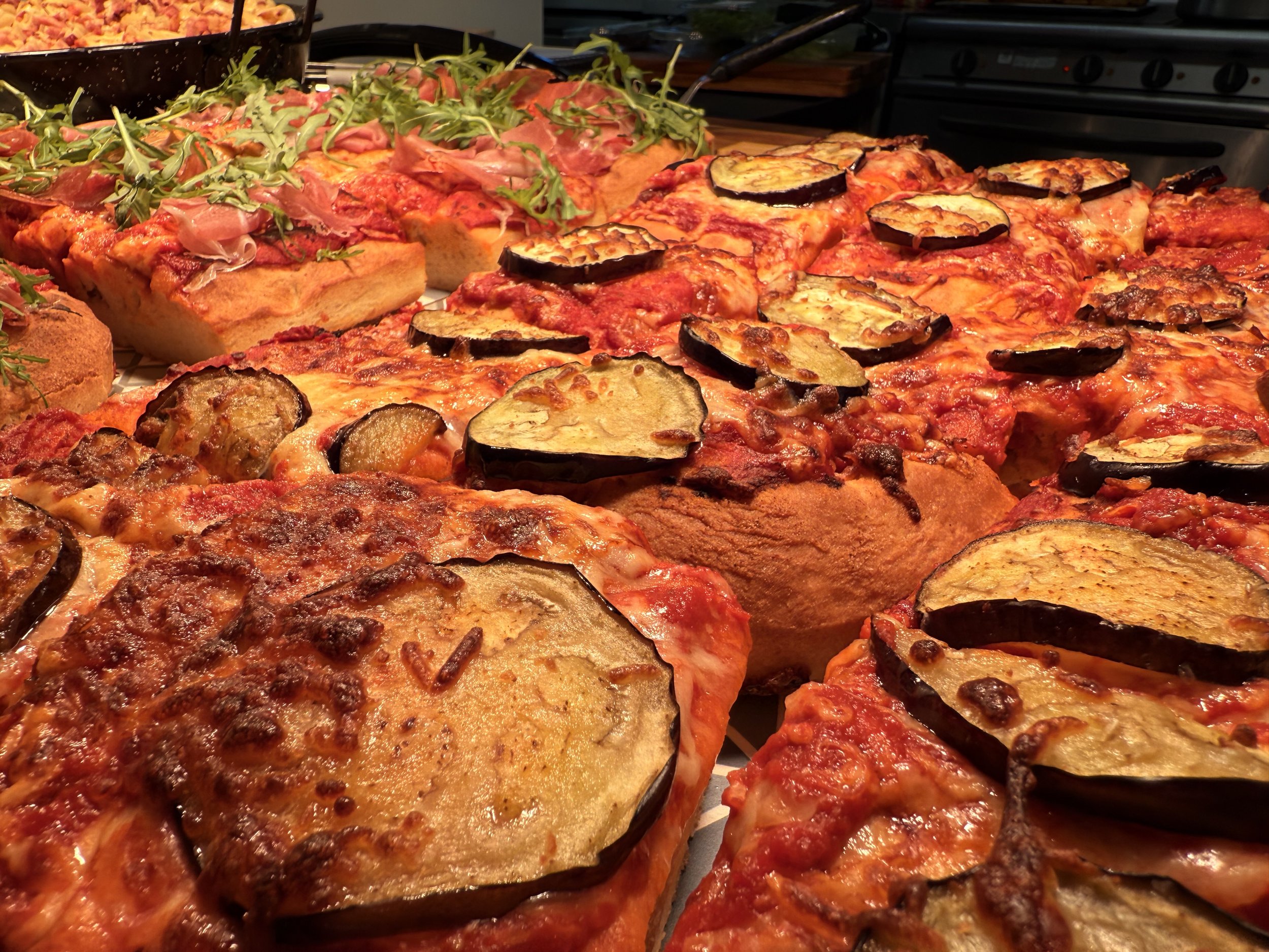 Multiple homemade pizzas topped with eggplant and other vegetables, arranged on a tray.