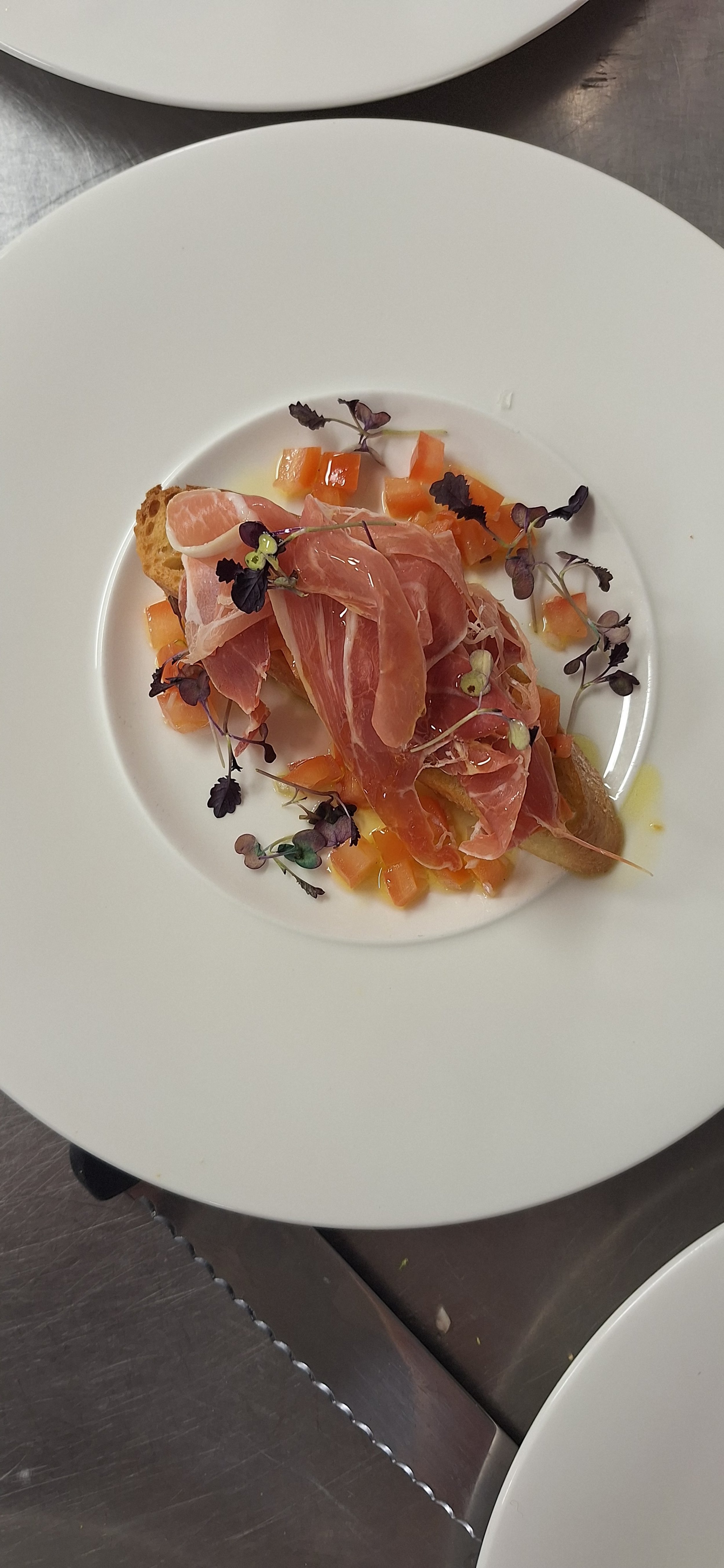 A plate with sliced cured ham, chopped orange vegetables, and microgreens garnished on toasted bread.
