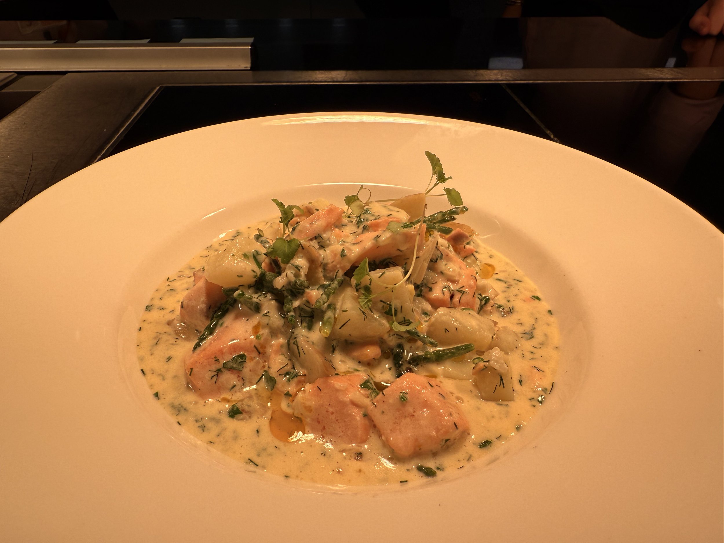 Plate of salmon and vegetables in a creamy herb sauce with microgreens garnish.