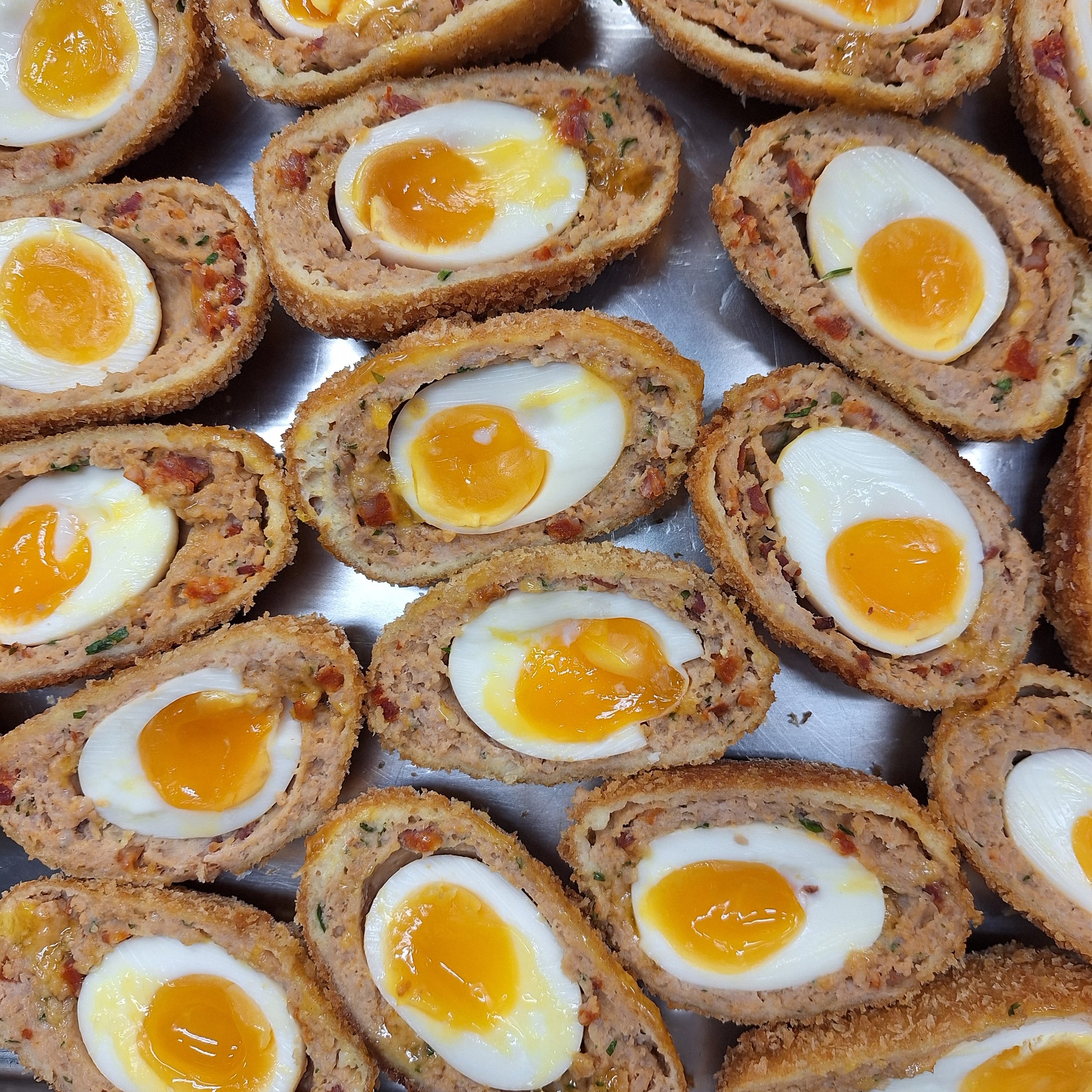 Deviled eggs made with a ground meat mixture, topped with halved soft-boiled eggs, arranged on a metal tray.