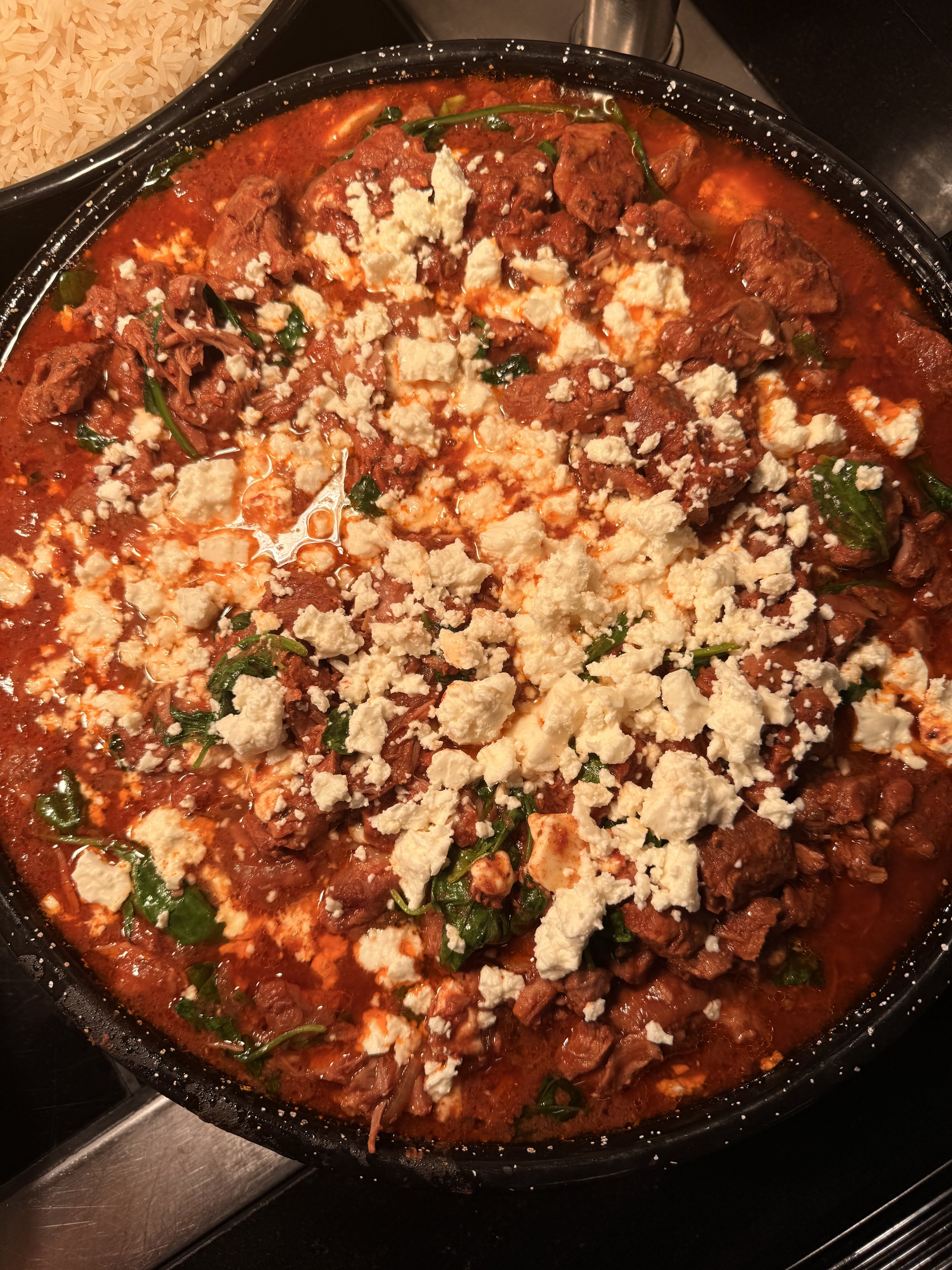 A skillet of cooked chili with crumbled cheese on top, garnished with green herbs.