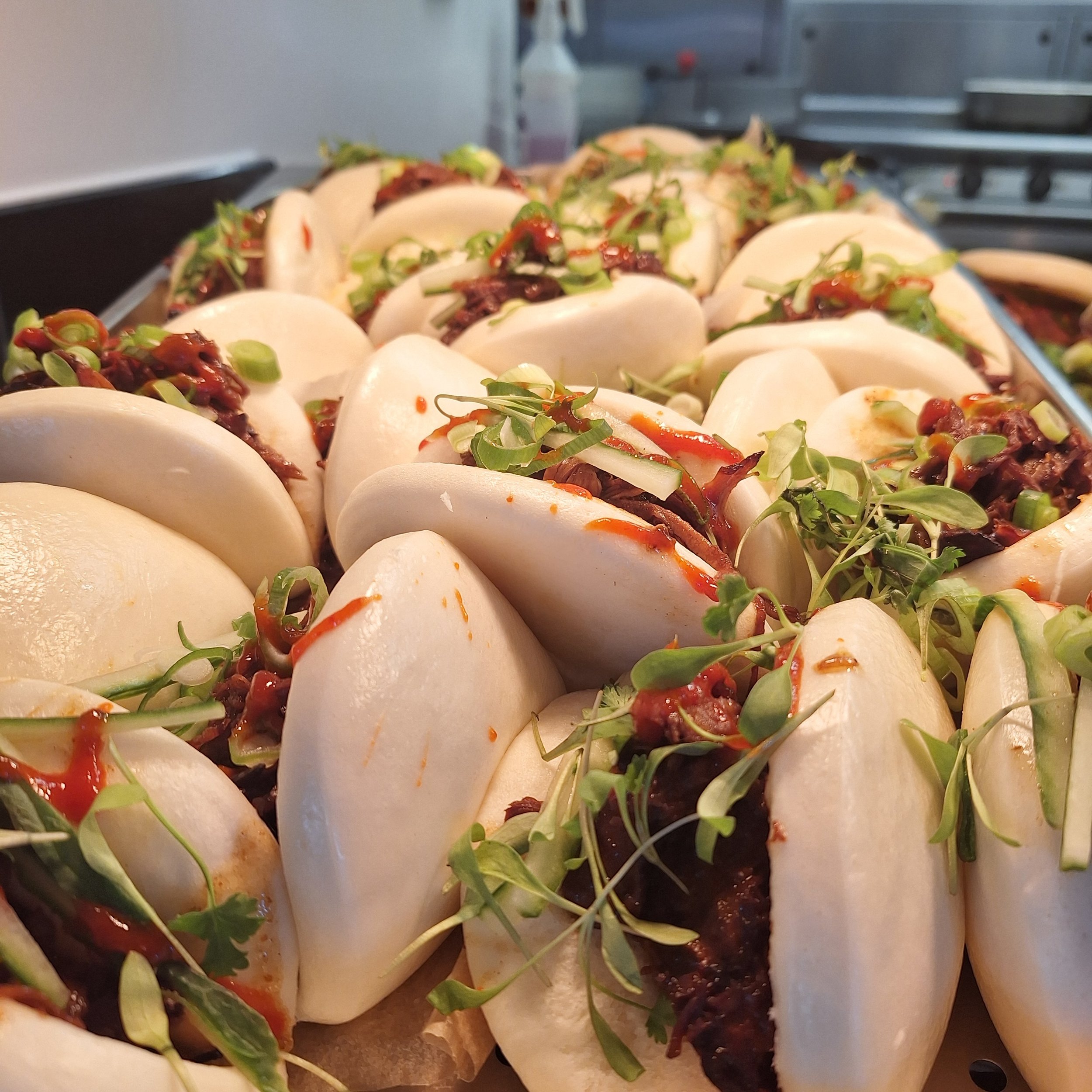 Close-up of several steamed pork buns filled with shredded meat, garnished with green sprouts and drizzled with sauce.