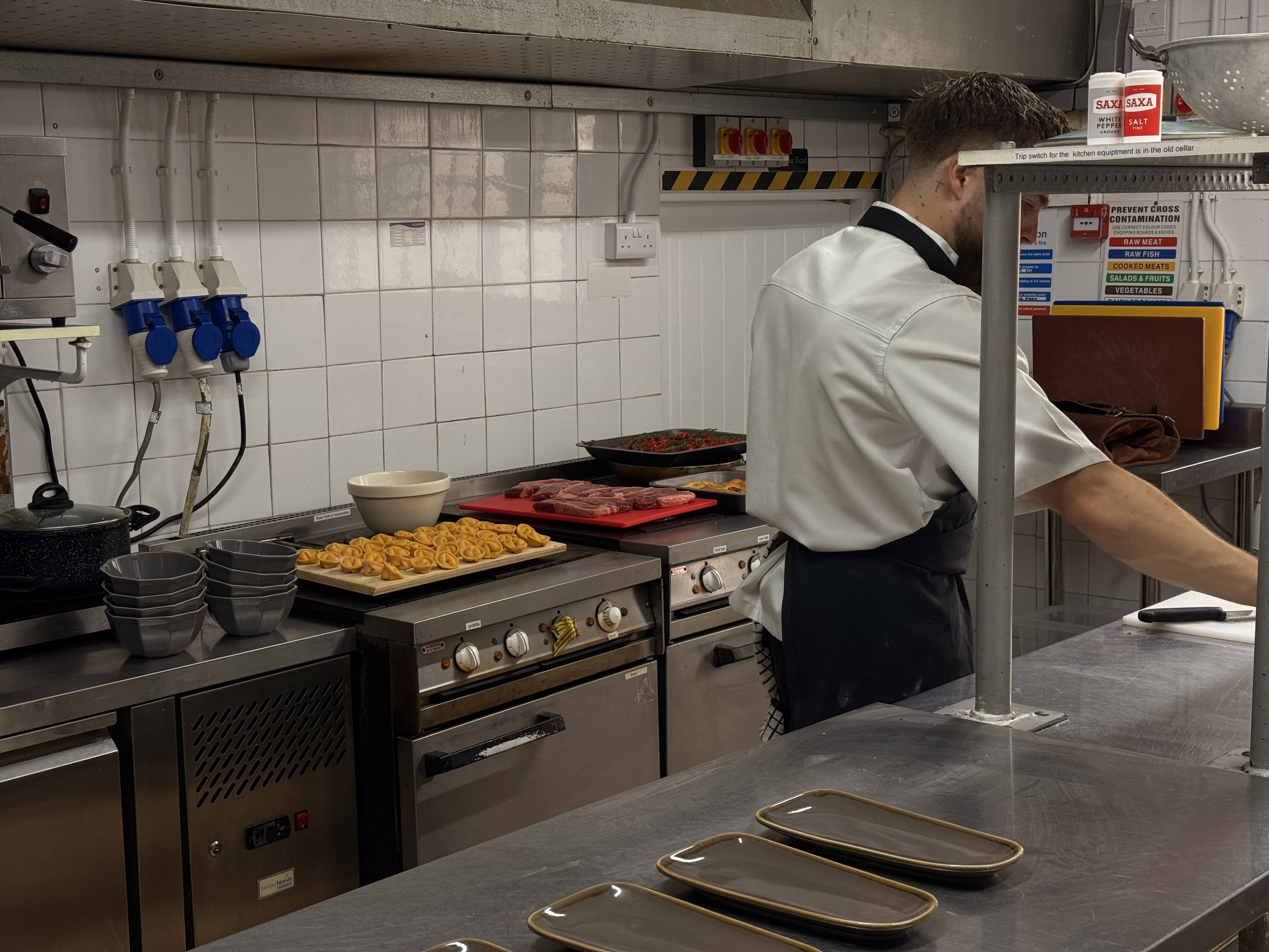 Chef preparing food in a commercial kitchen with various dishes and utensils on the counters.